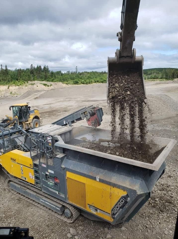 Une excavatrice déverse de la terre dans un concasseur de roche mobile jaune et noir dans une carrière.