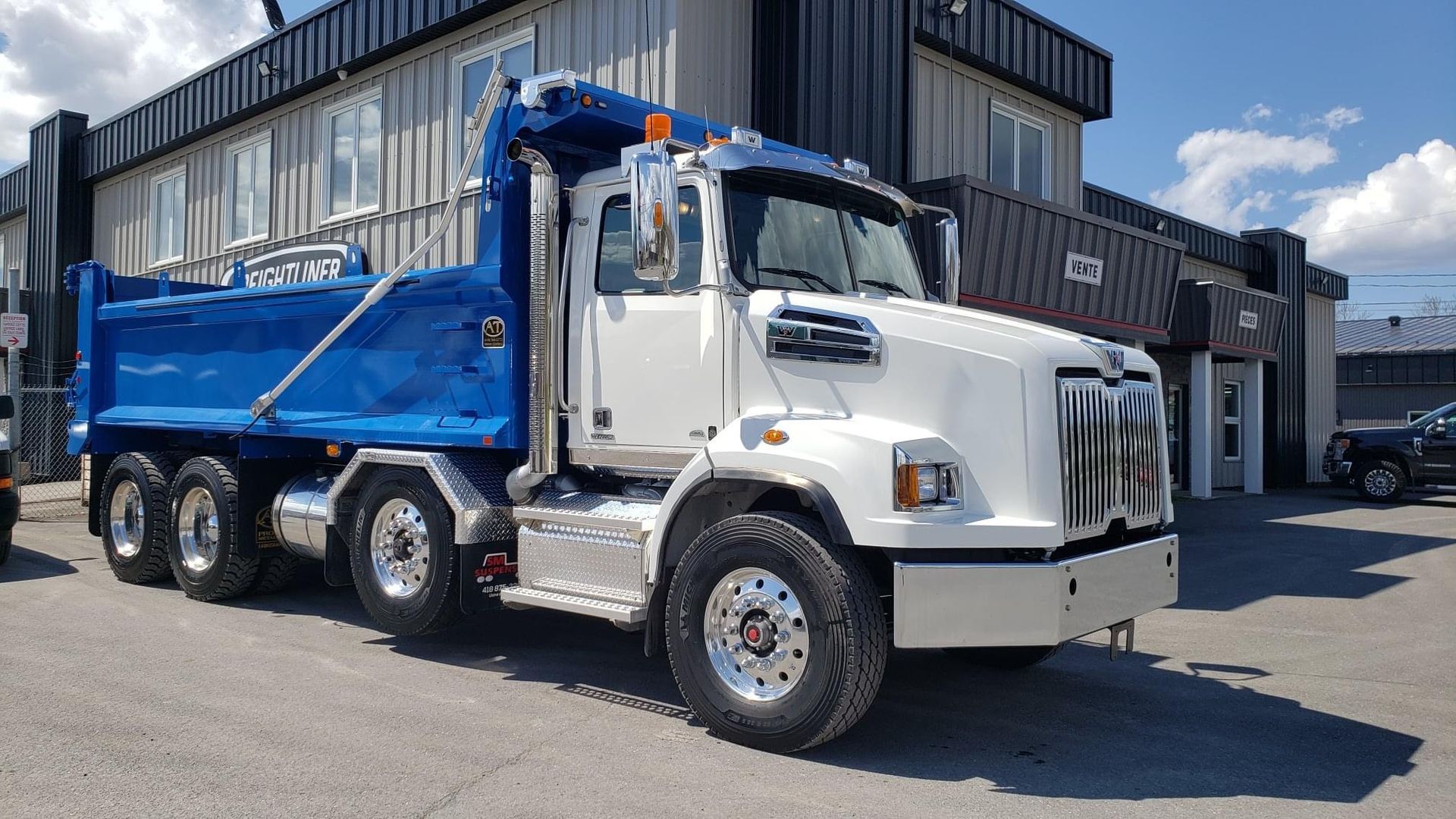 Camion à benne basculante blanc et bleu garé à l'extérieur d'un bâtiment.