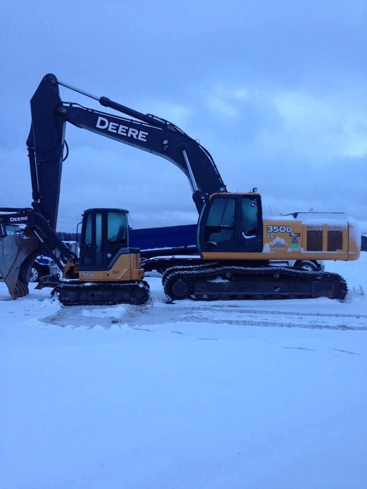 Deux excavatrices John Deere sur un sol enneigé sous un ciel nuageux.