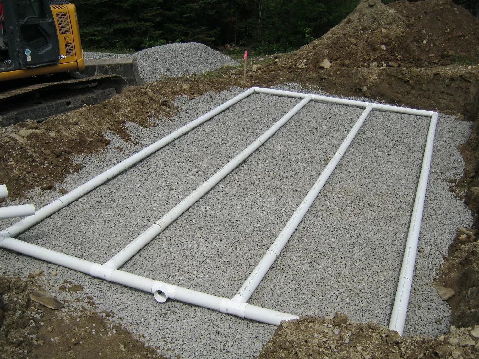 Fosse remplie de gravier avec des tuyaux en PVC blanc formant une grille pour une fosse septique.