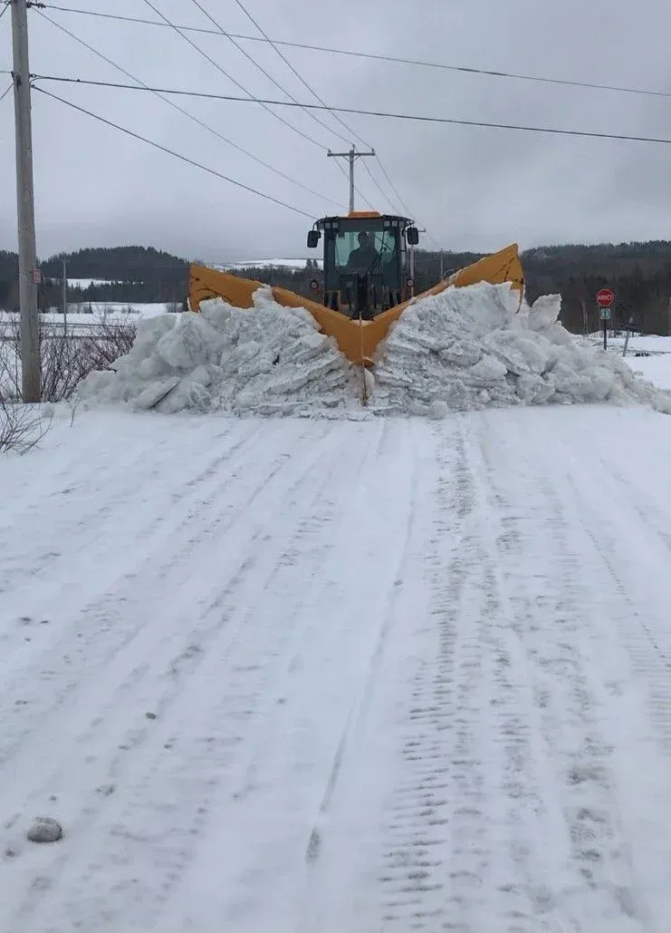 Un chasse-neige dégageant une route enneigée, poussant un gros tas de neige devant lui.