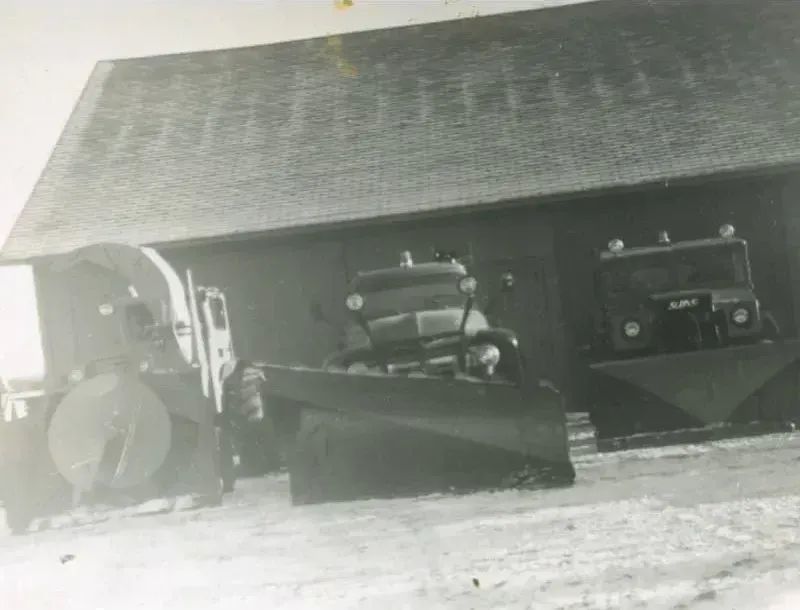 Trois chasse-neige d'époque stationnés sous un hangar.