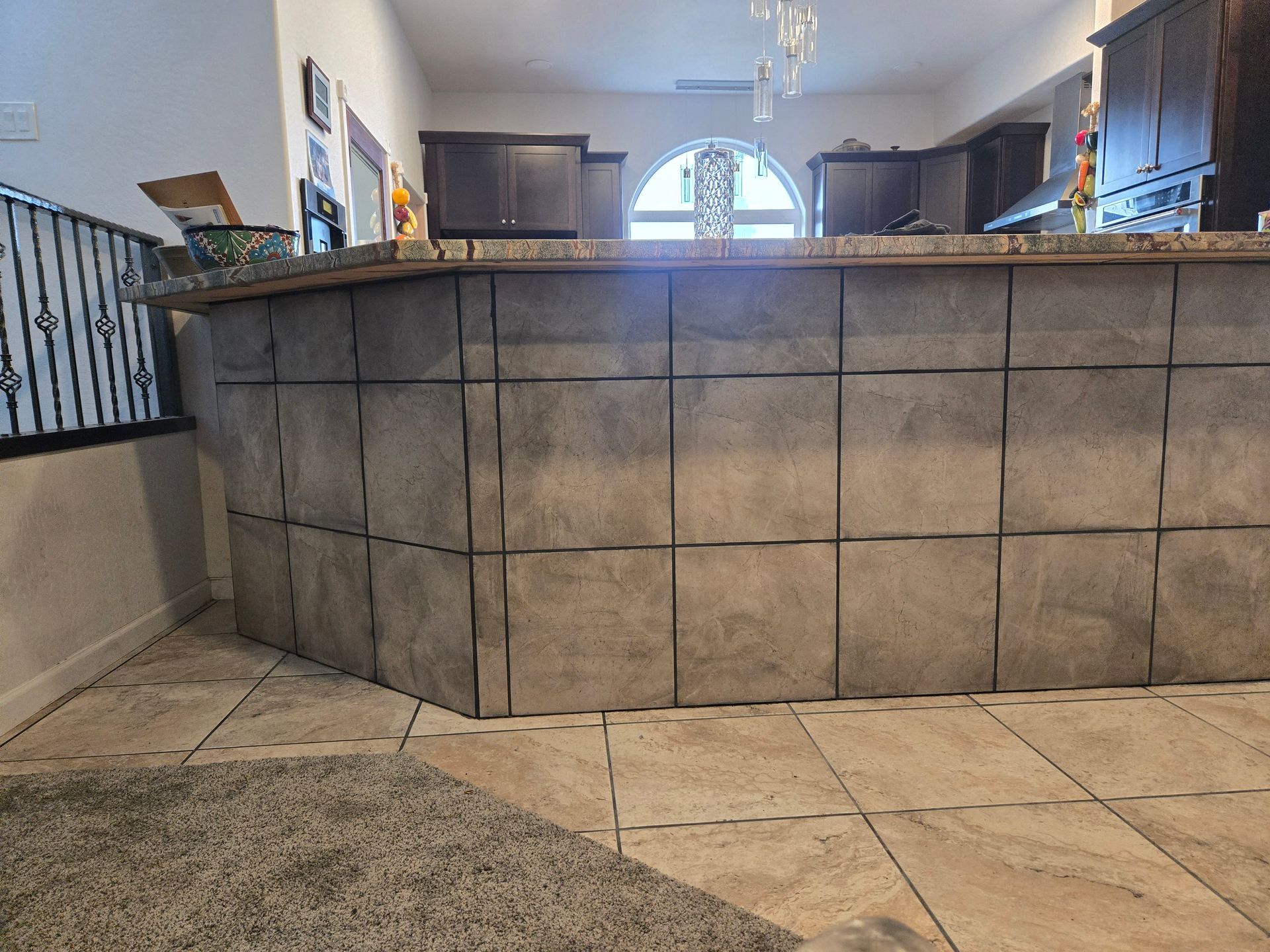 Indoor kitchen with a large gray tiled breakfast bar and tan stone floor.