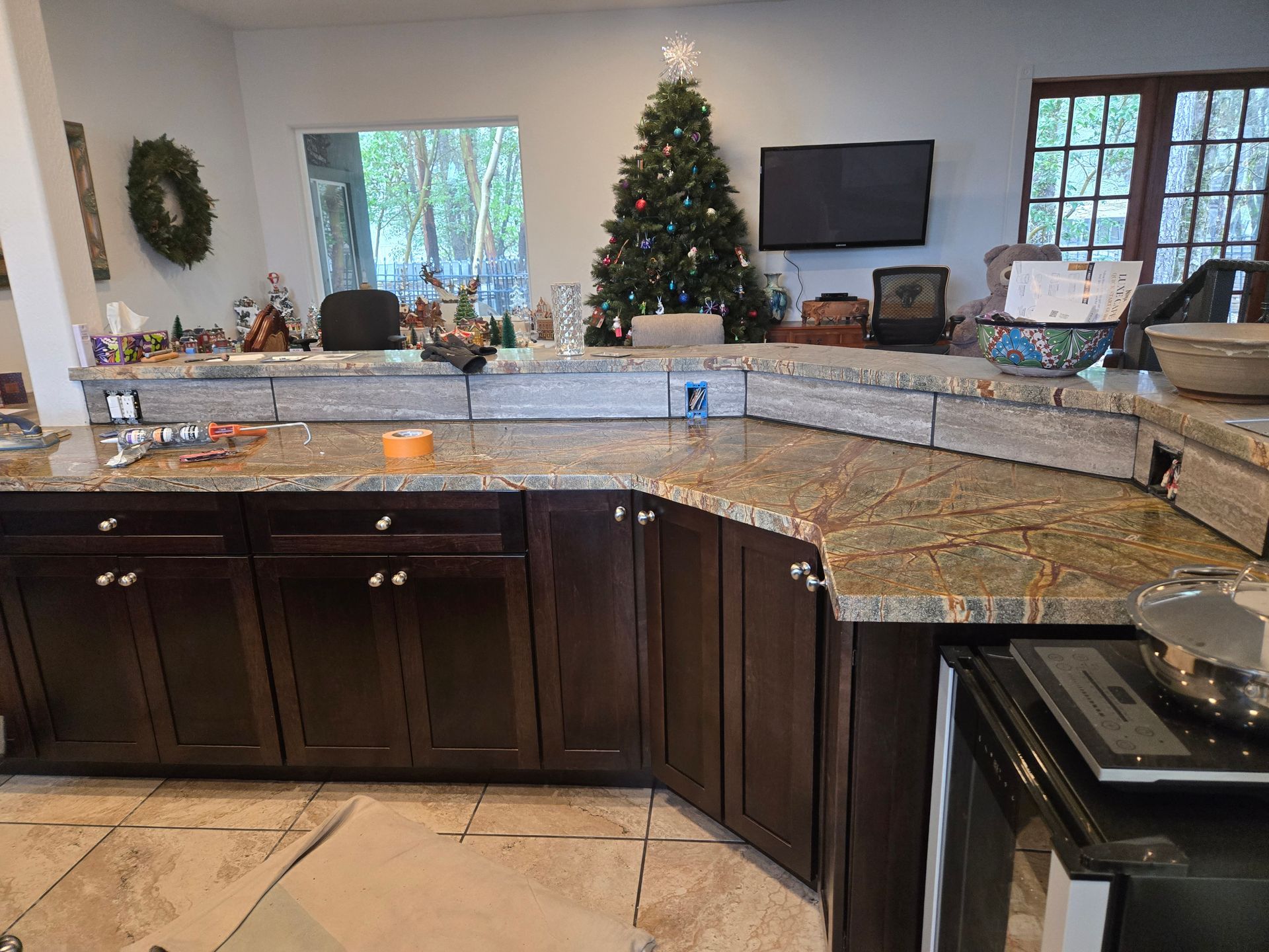 Holiday-decorated kitchen with granite island, dark cabinets, and a Christmas tree by the window