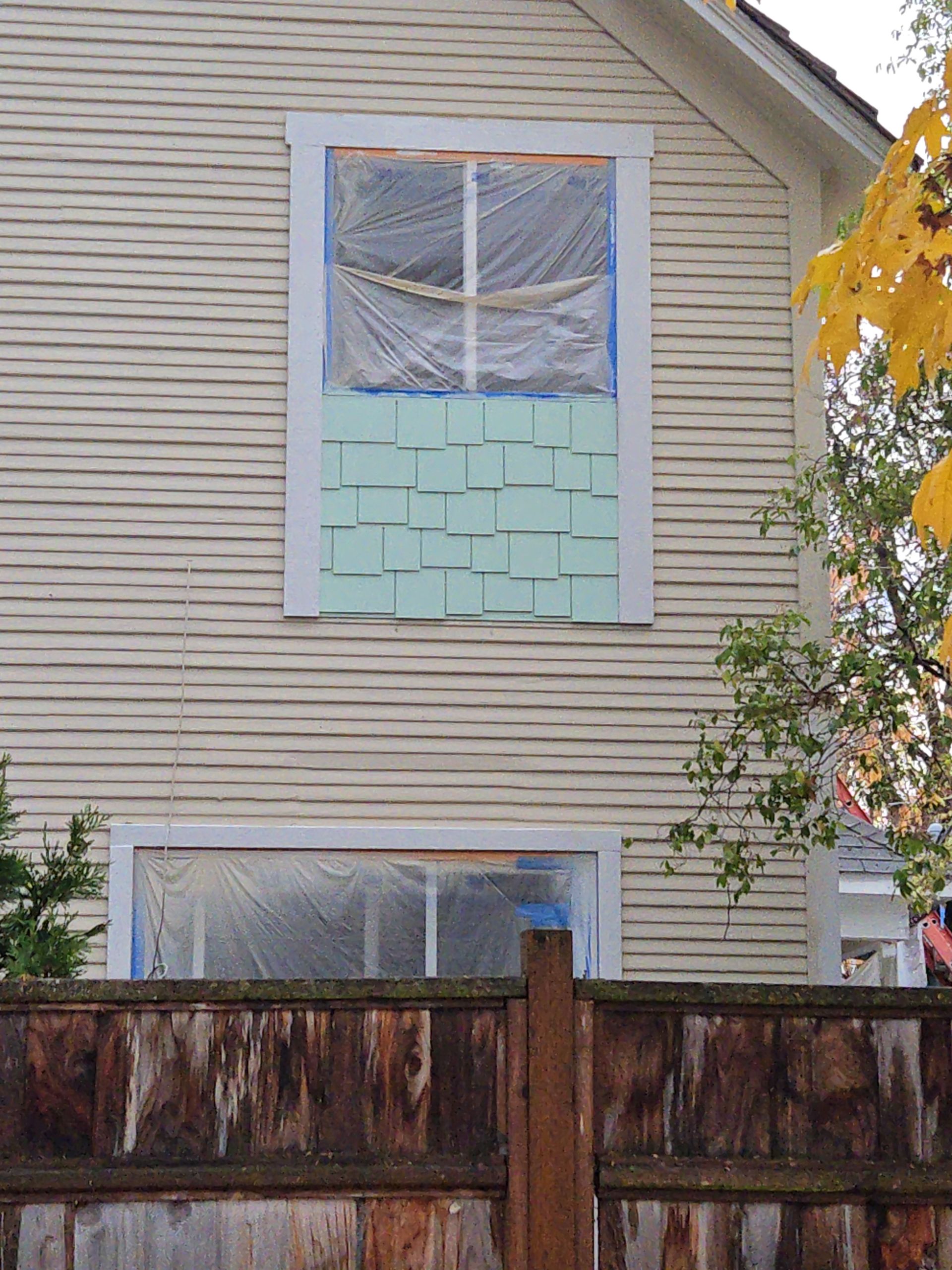 House exterior with a boarded-up upper window and a wooden fence in front