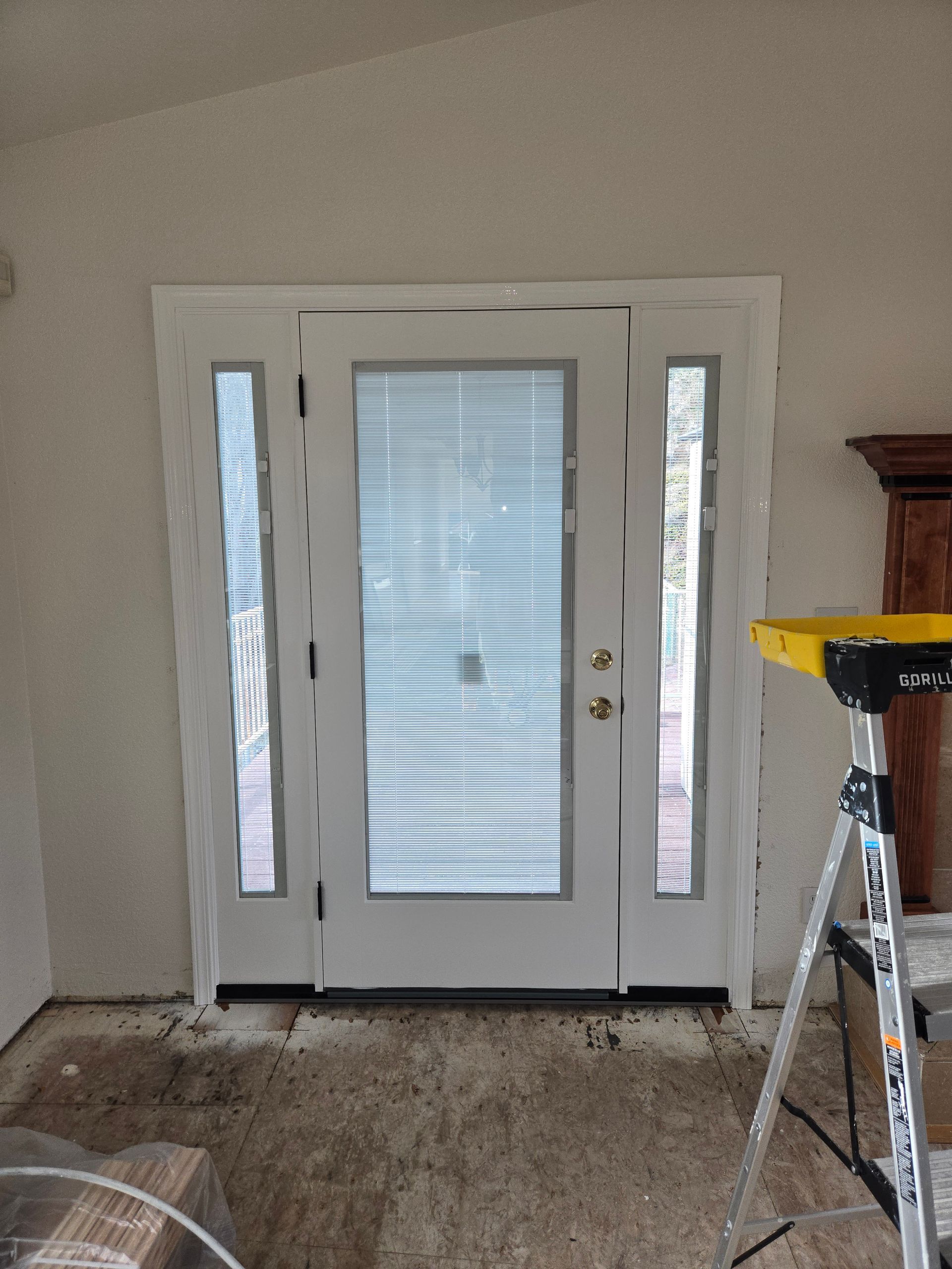 White front door with sidelights and blinds in an unfinished room with a ladder nearby
