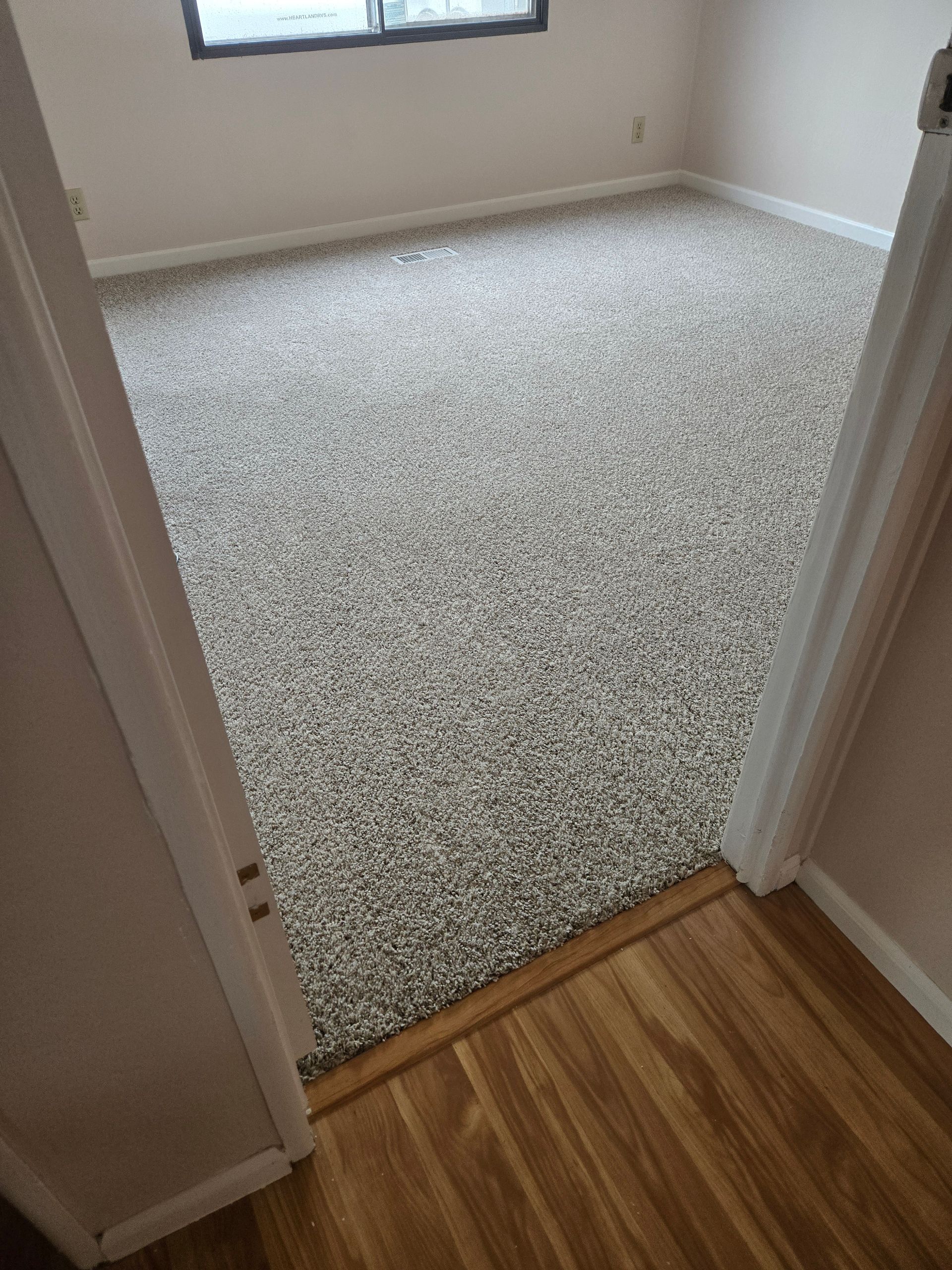 Doorway view into an empty beige room with light gray carpet and a window.