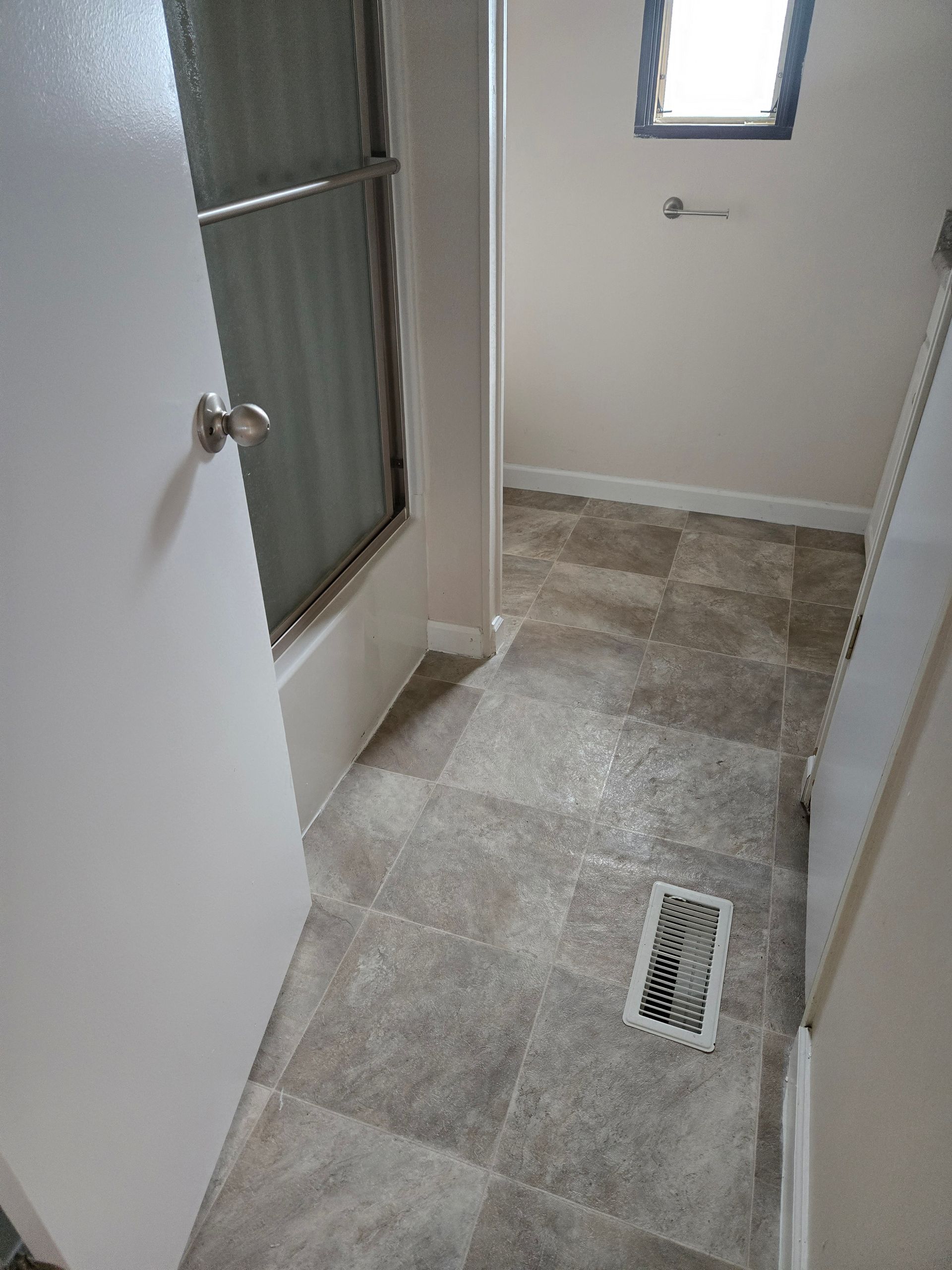 Narrow hallway with gray tile floor, white walls, a window, and a floor vent.
