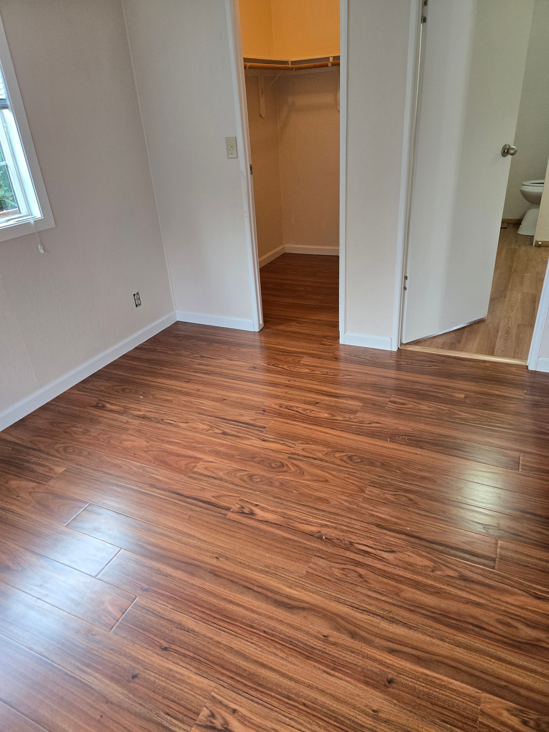 Empty room with glossy wood floors, white walls, a closet, and a window.