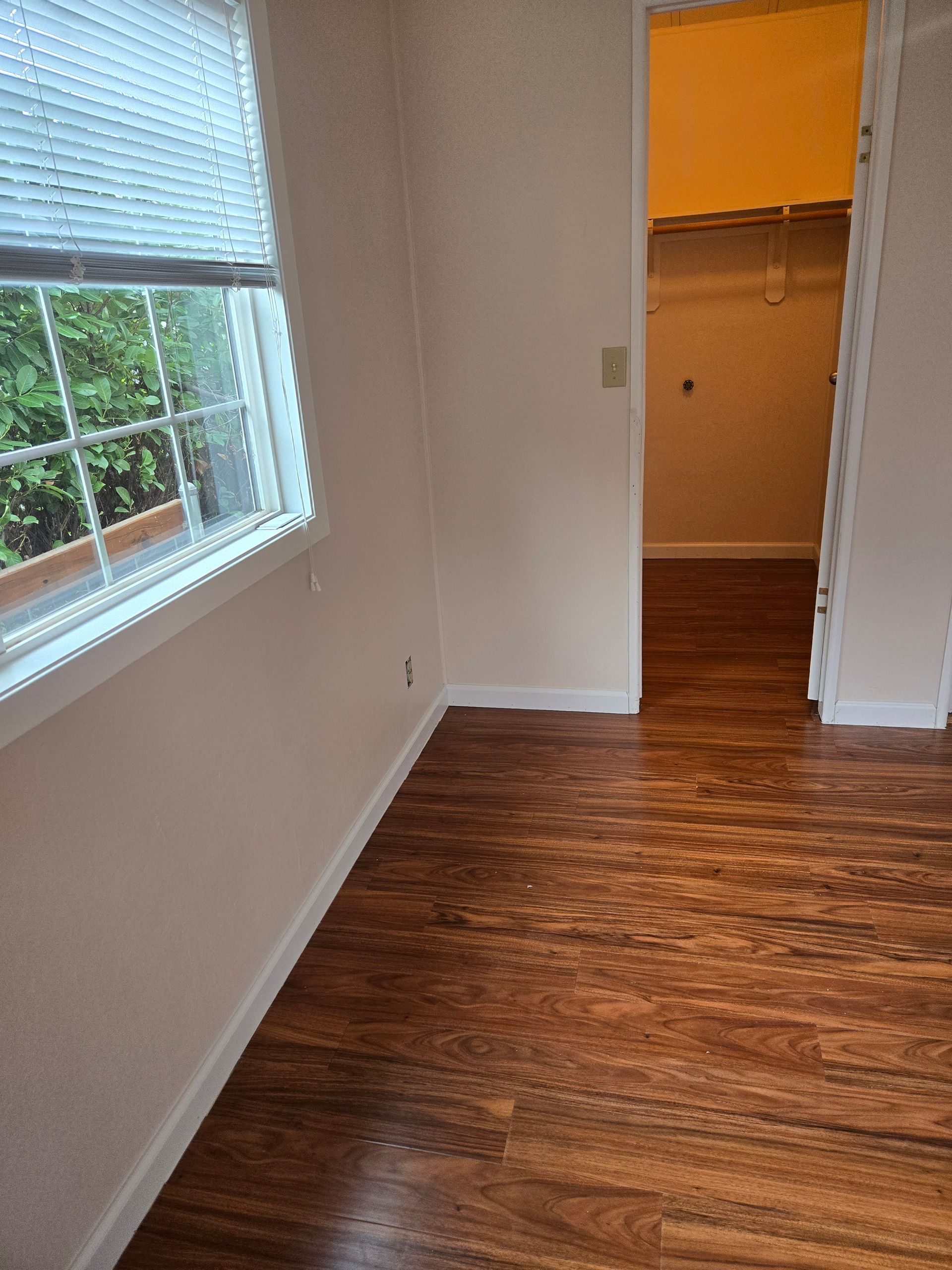 Empty room with white walls, wood floor, a window on the left, and an open closet doorway.