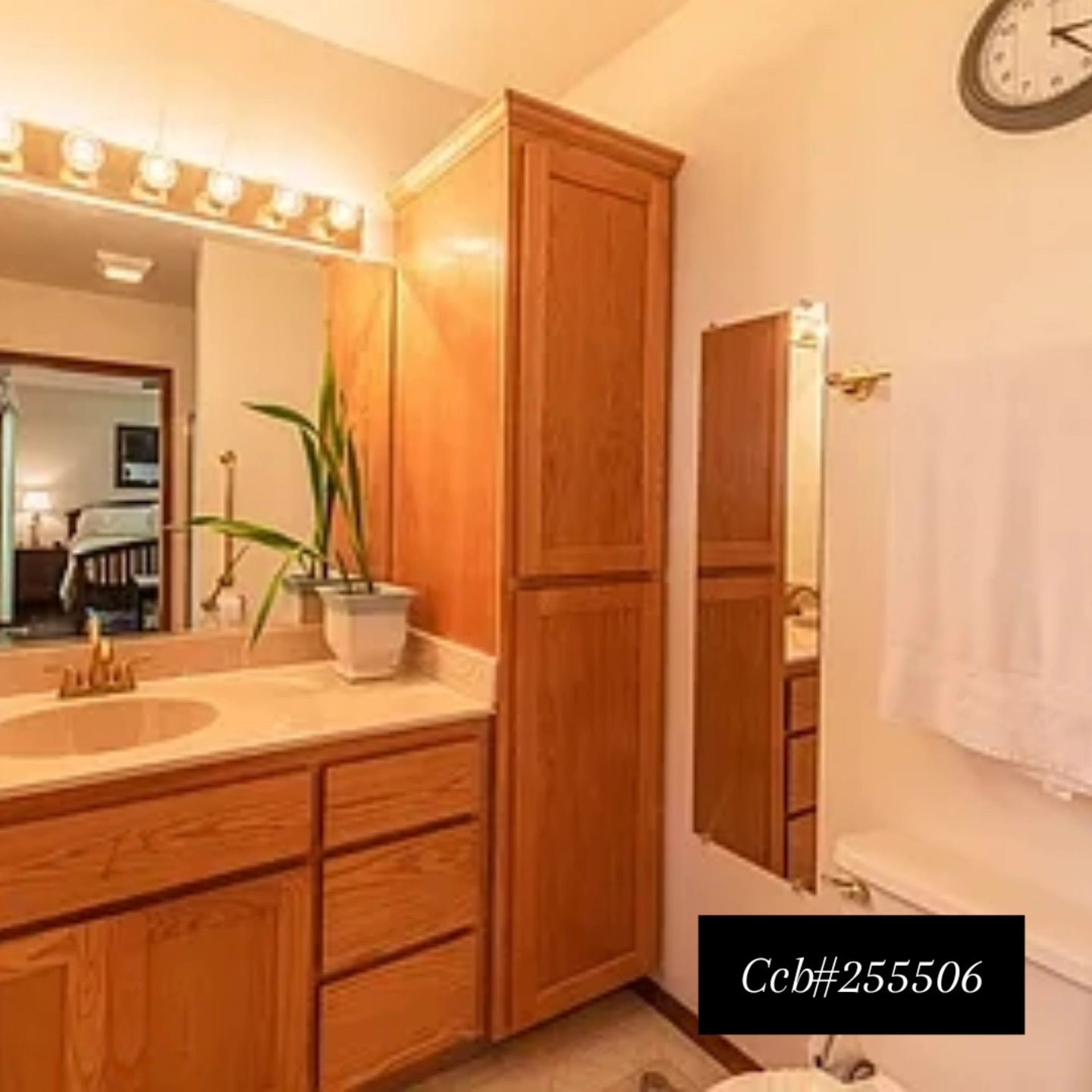 Warm bathroom with wooden vanity, large mirror, towel rack, tall cabinet, and wall clock.