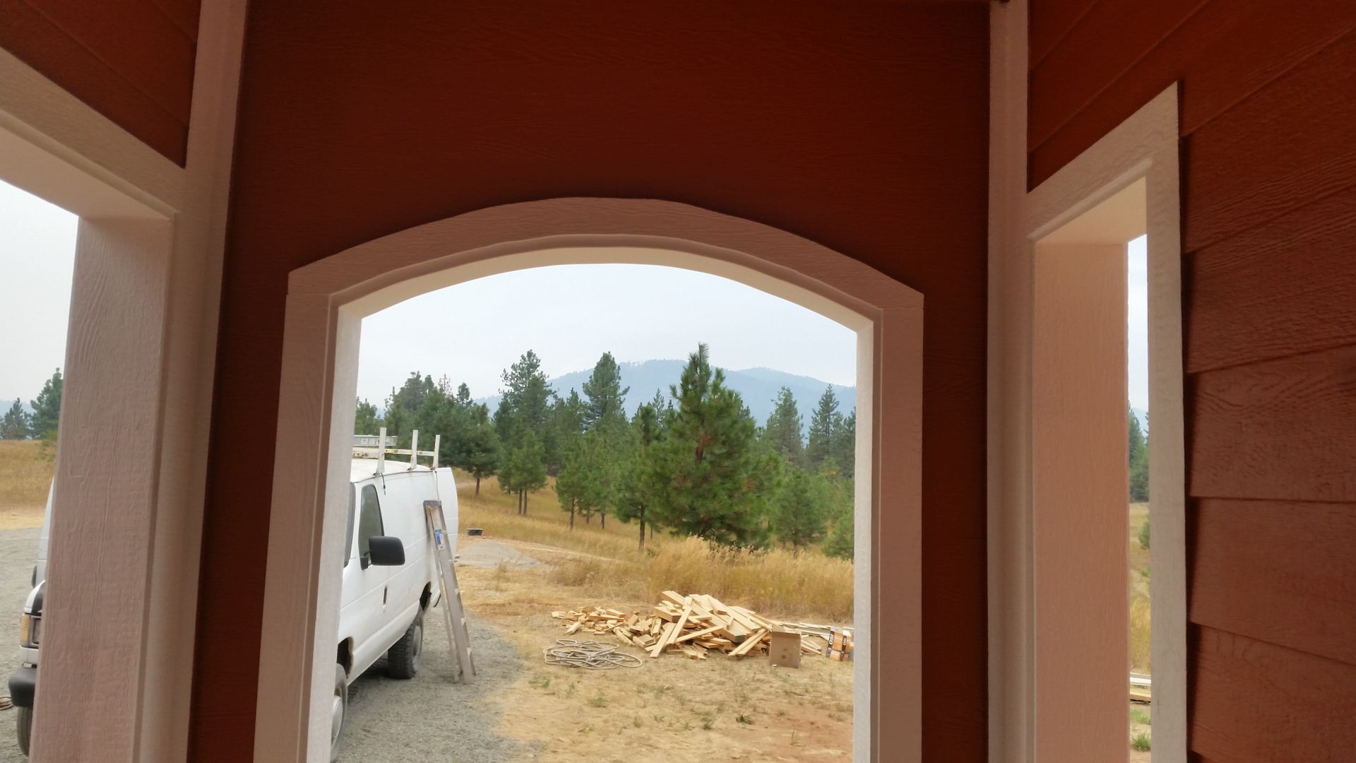 White RV seen through an arched doorway, with a wooded landscape and piles of dirt outside.