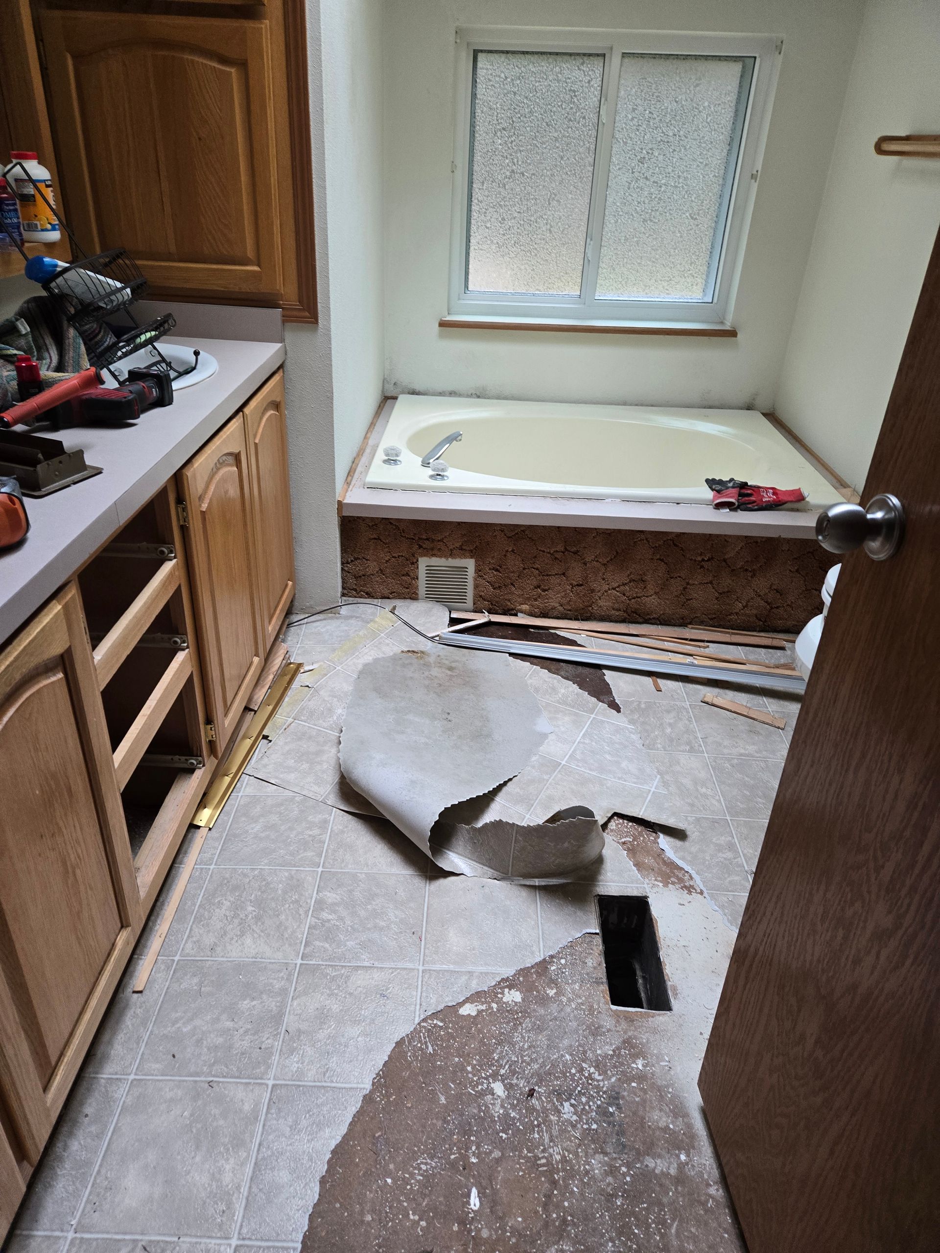 Damaged kitchen with torn flooring, debris on the floor, and a broken window above a tub alcove