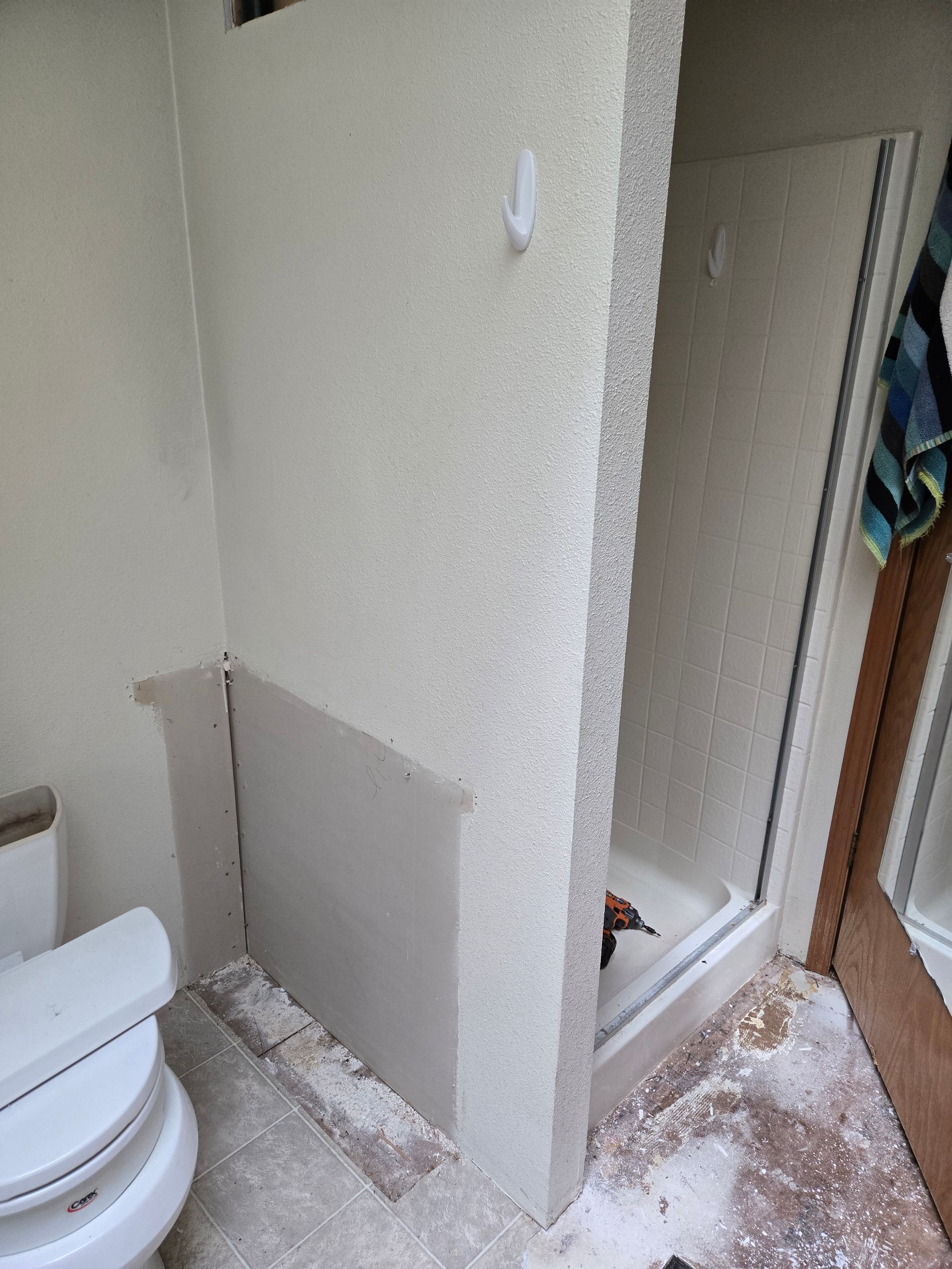 Bathroom with toilet and tiled shower area, floor and wall partially demolished with debris scattered.