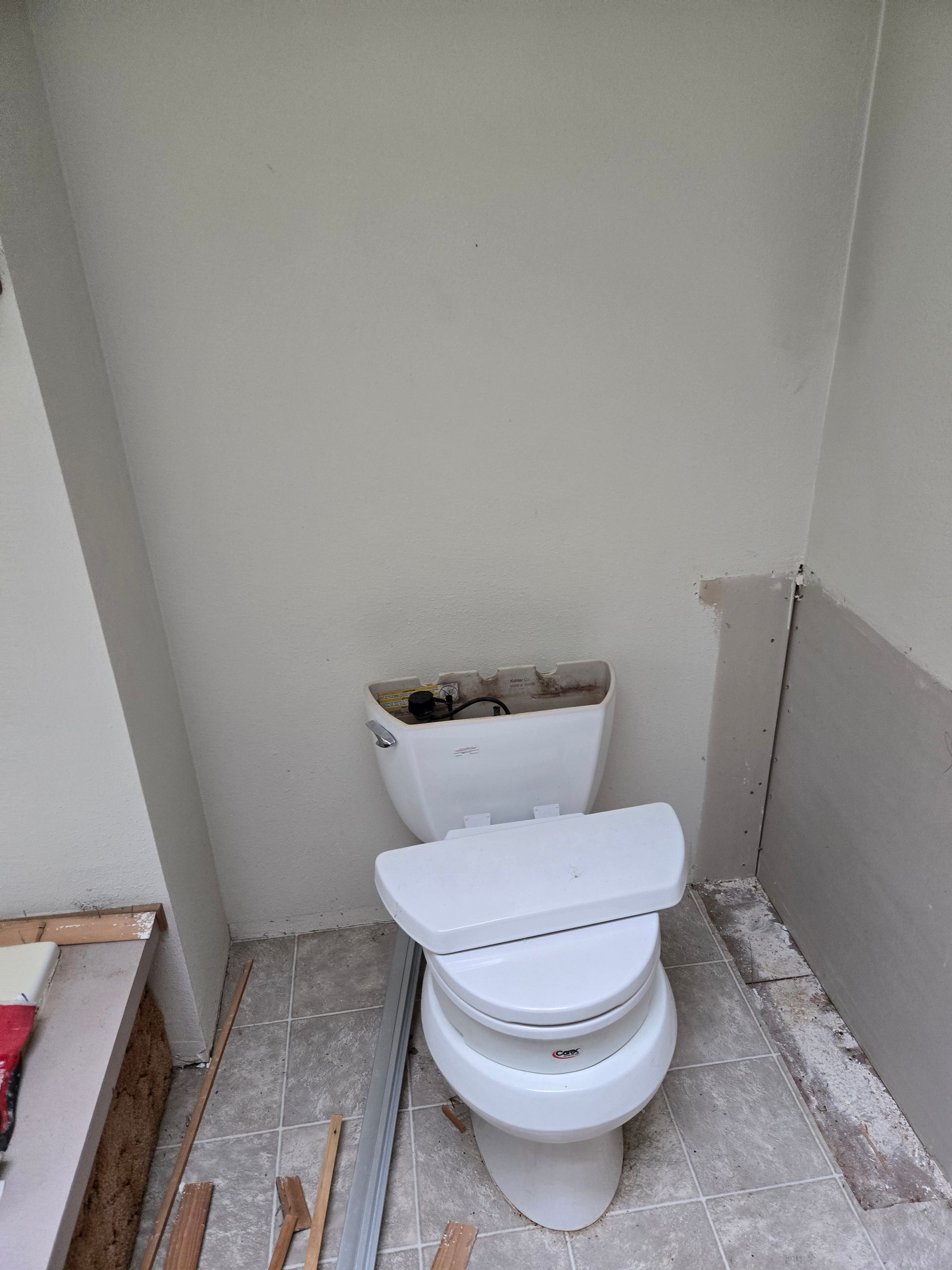 Partially installed toilet in a small unfinished bathroom with exposed flooring and walls