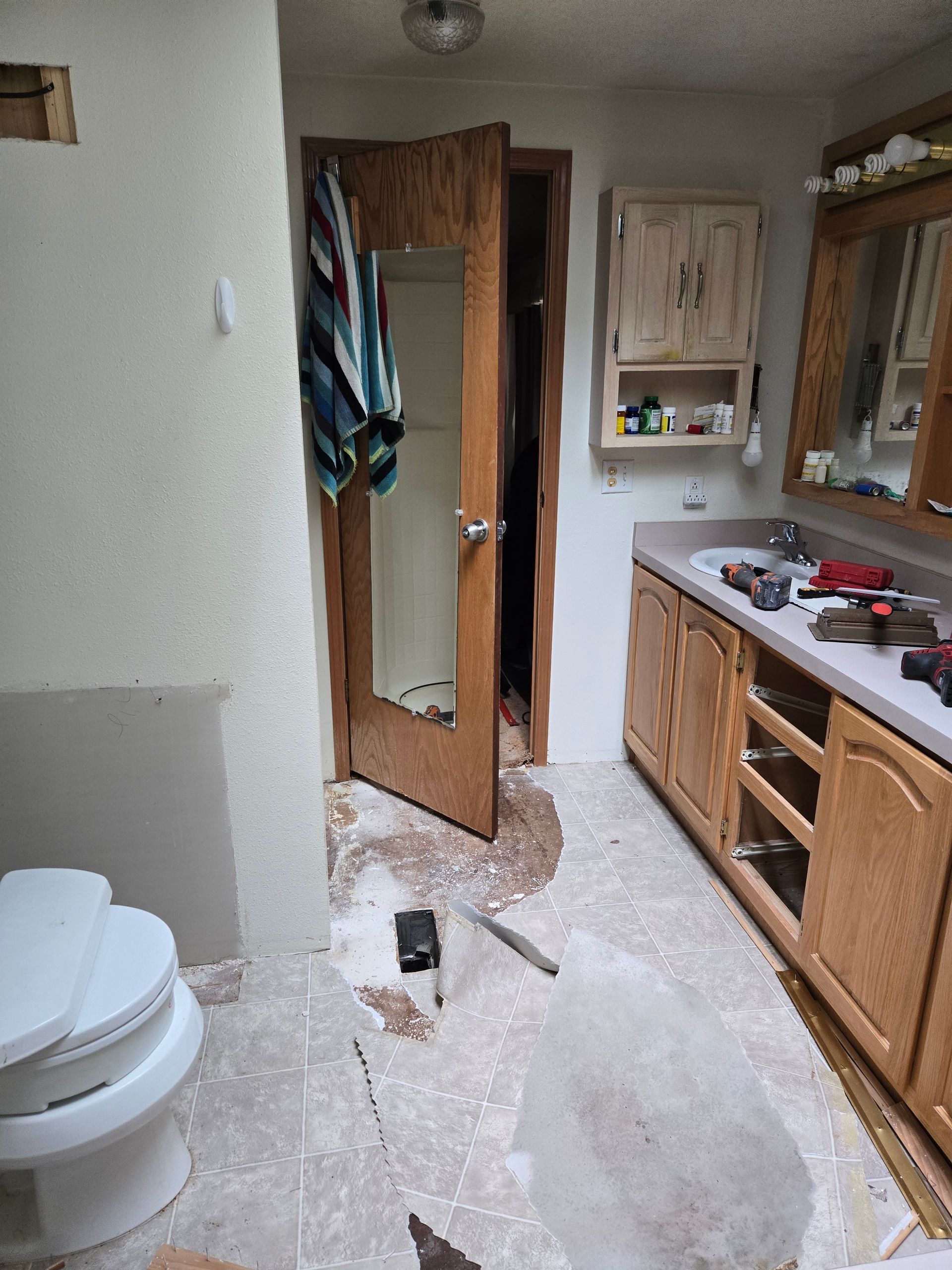 Small bathroom with a toilet, wood vanity, open door, and a broom on the floor.