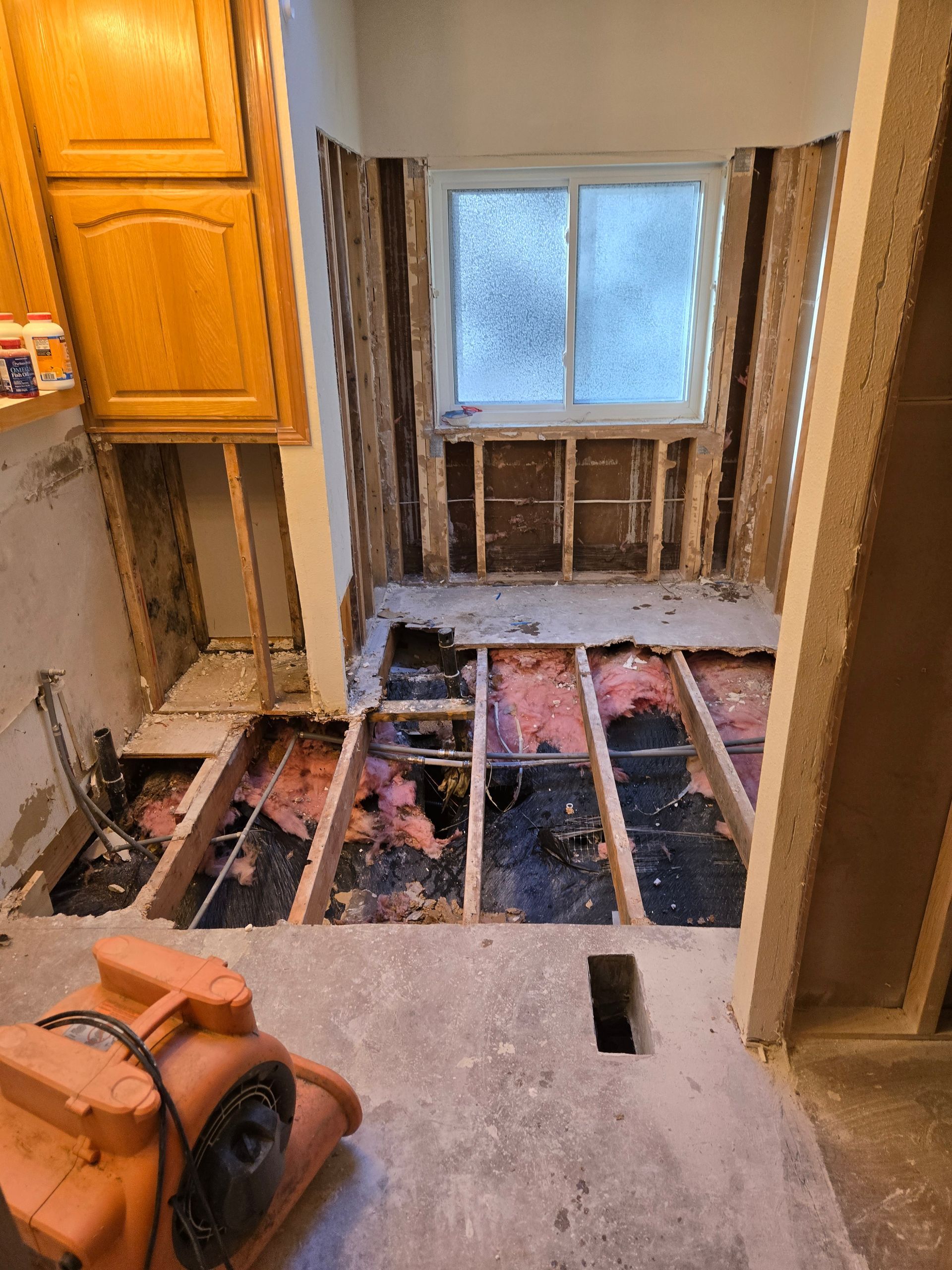 Kitchen under renovation with exposed floor joists, removed cabinets, and a window at the back.