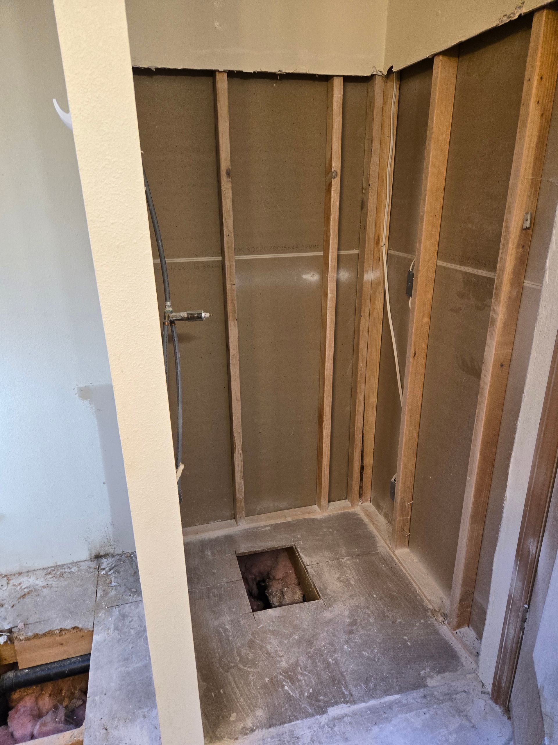 Partially demolished bathroom with exposed wall studs, concrete floor, and toilet flange opening