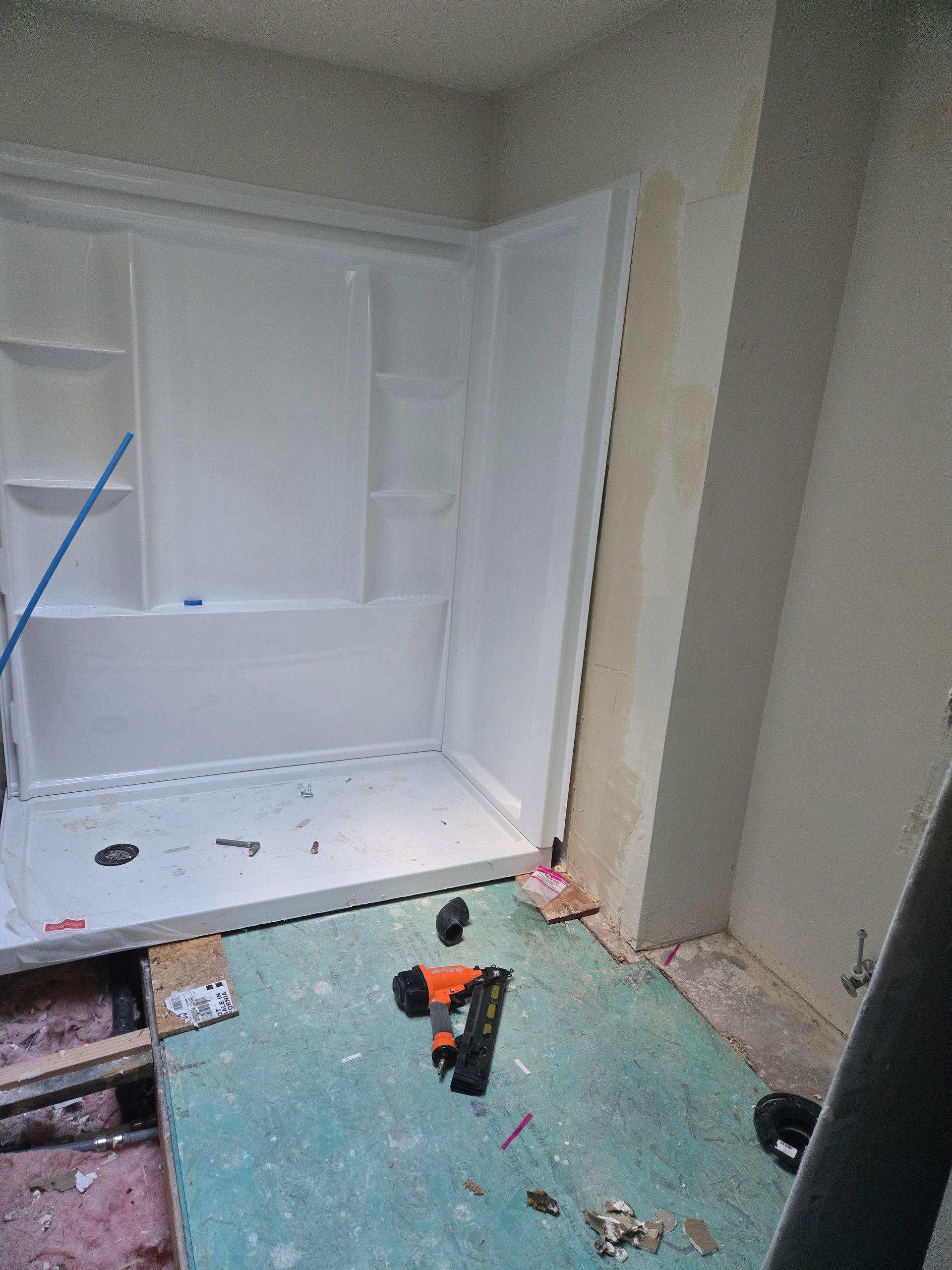 Partially renovated bathroom with white tub, green floor, and a drill on the floor