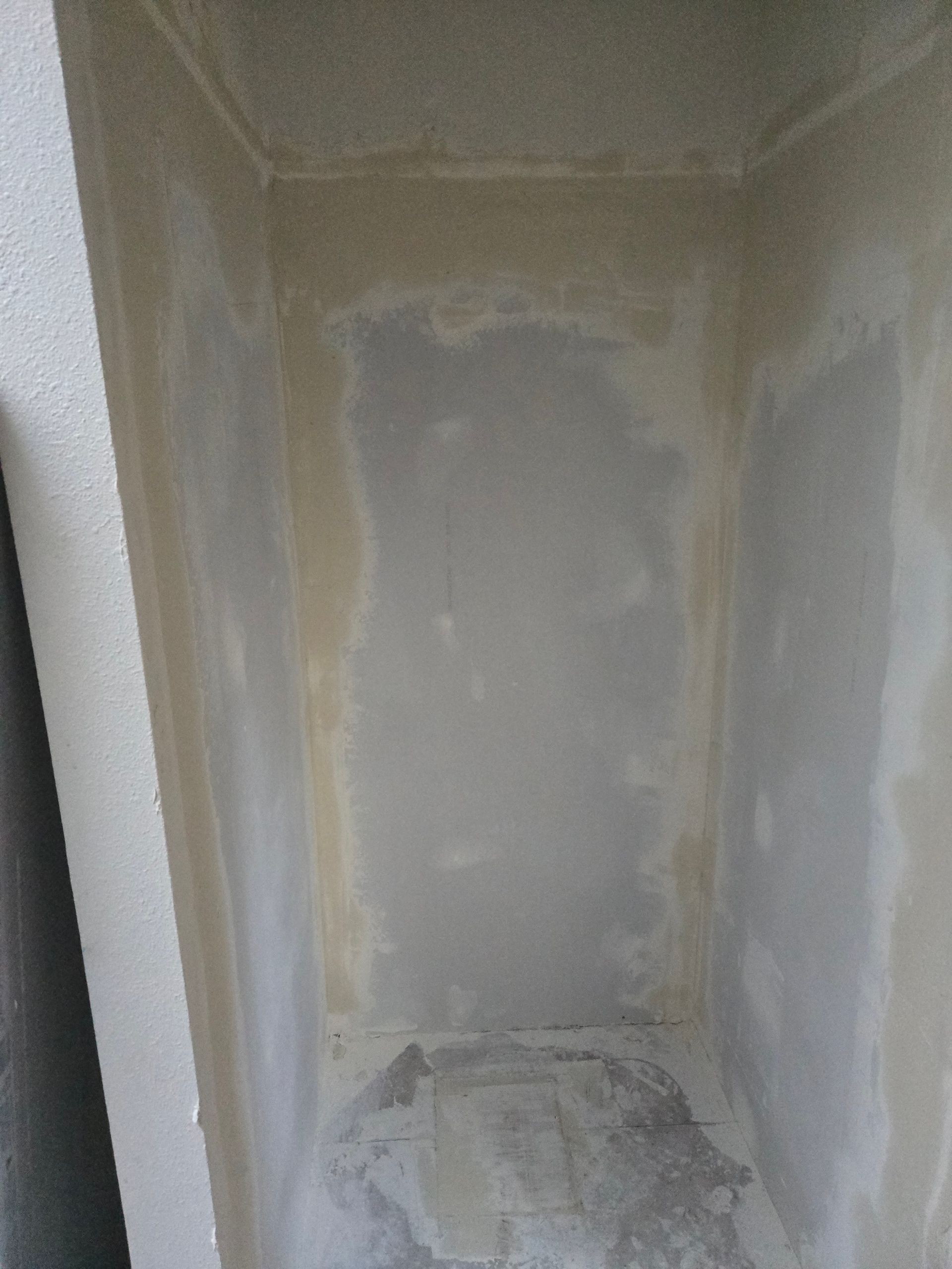 Narrow unfinished drywall alcove with patched seams and a rough concrete floor.