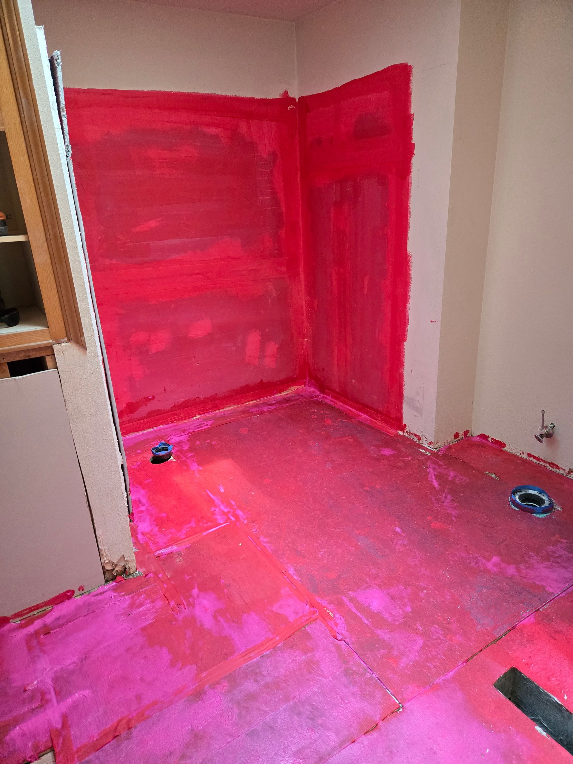 Small room corner with walls and floor heavily coated in bright pink paint or primer