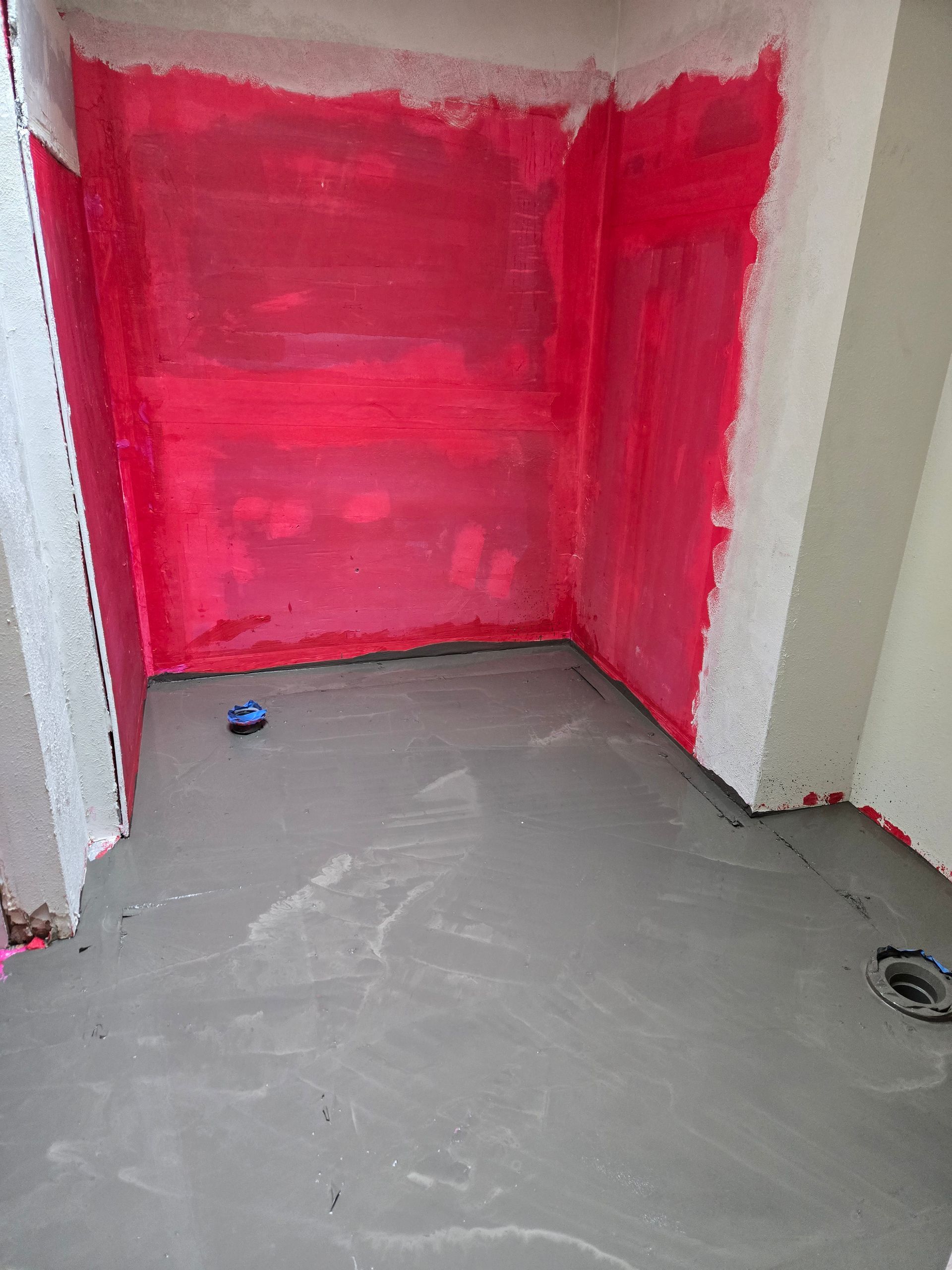 Small unfinished room with red painted walls, gray floor, and a blue object on the floor.