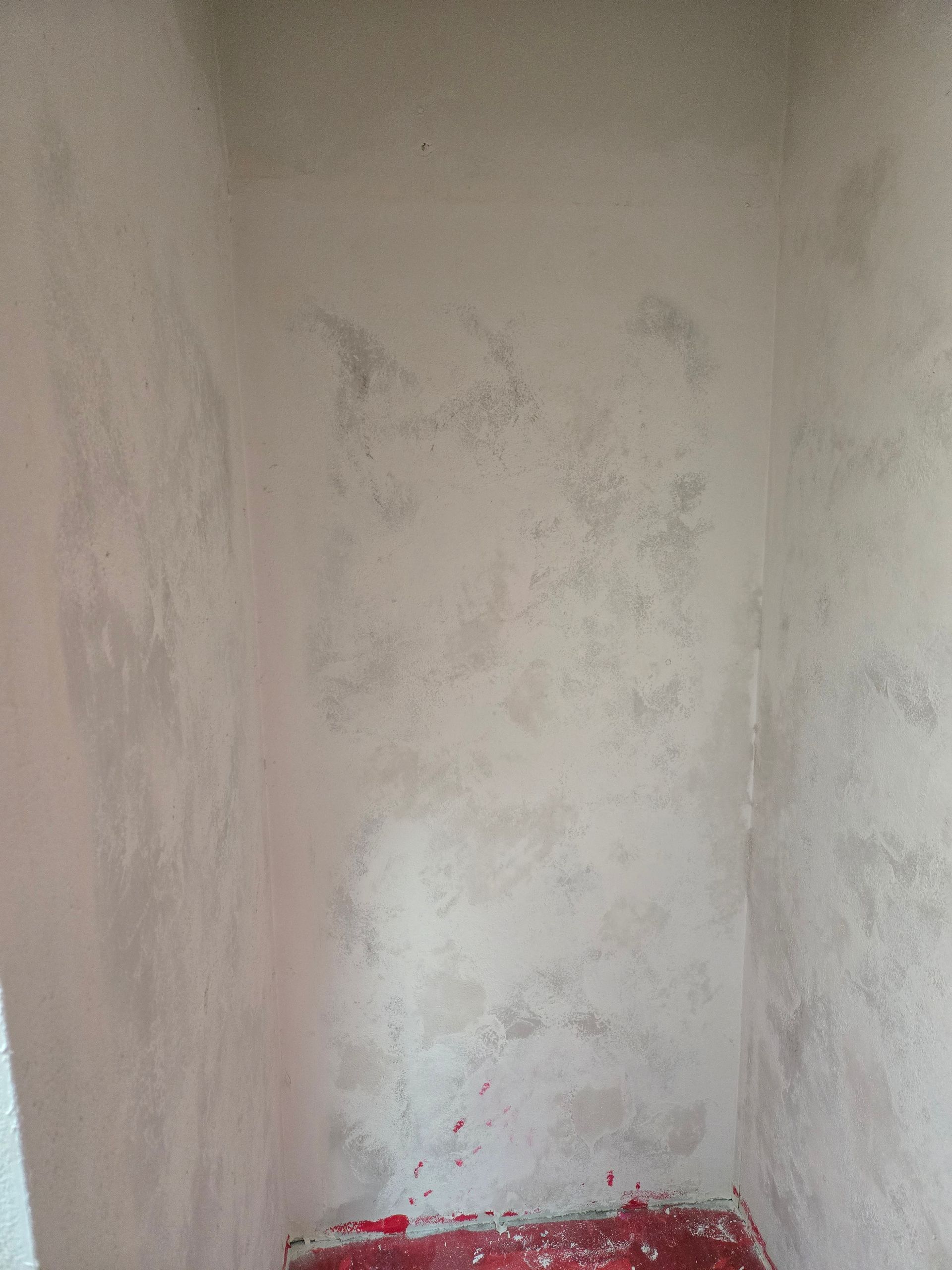 Stained white corner wall with mold spots and red debris along the floor.