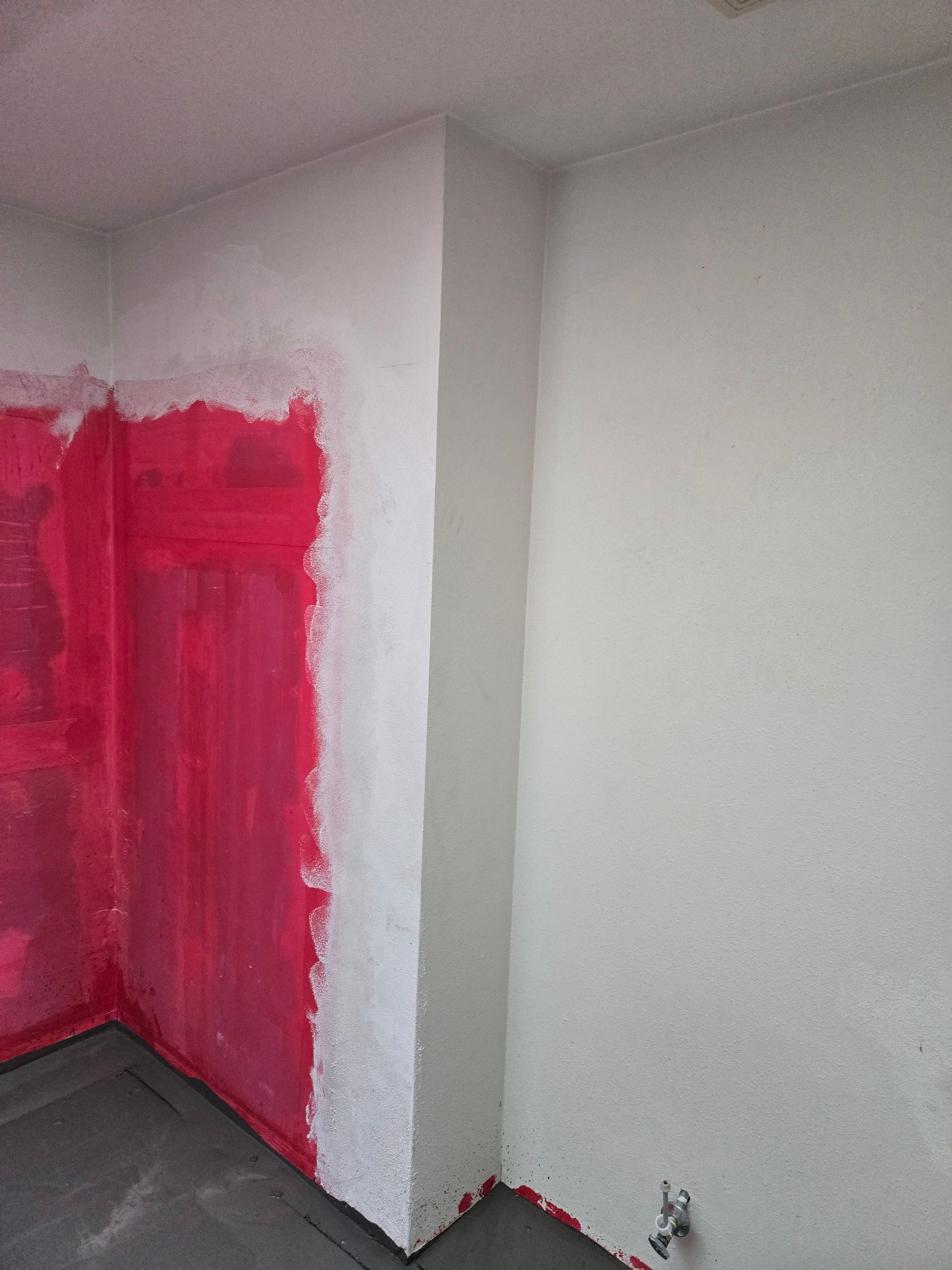 Partially painted room corner with bright pink wall paint and a white wall outlet near the floor