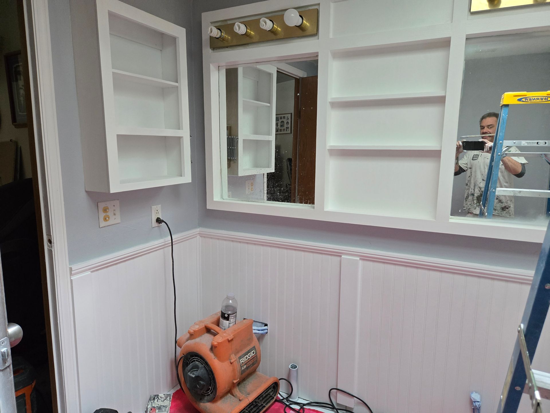 Small room with open white cabinets, mirror, radiator, and an orange floor polisher on the floor.