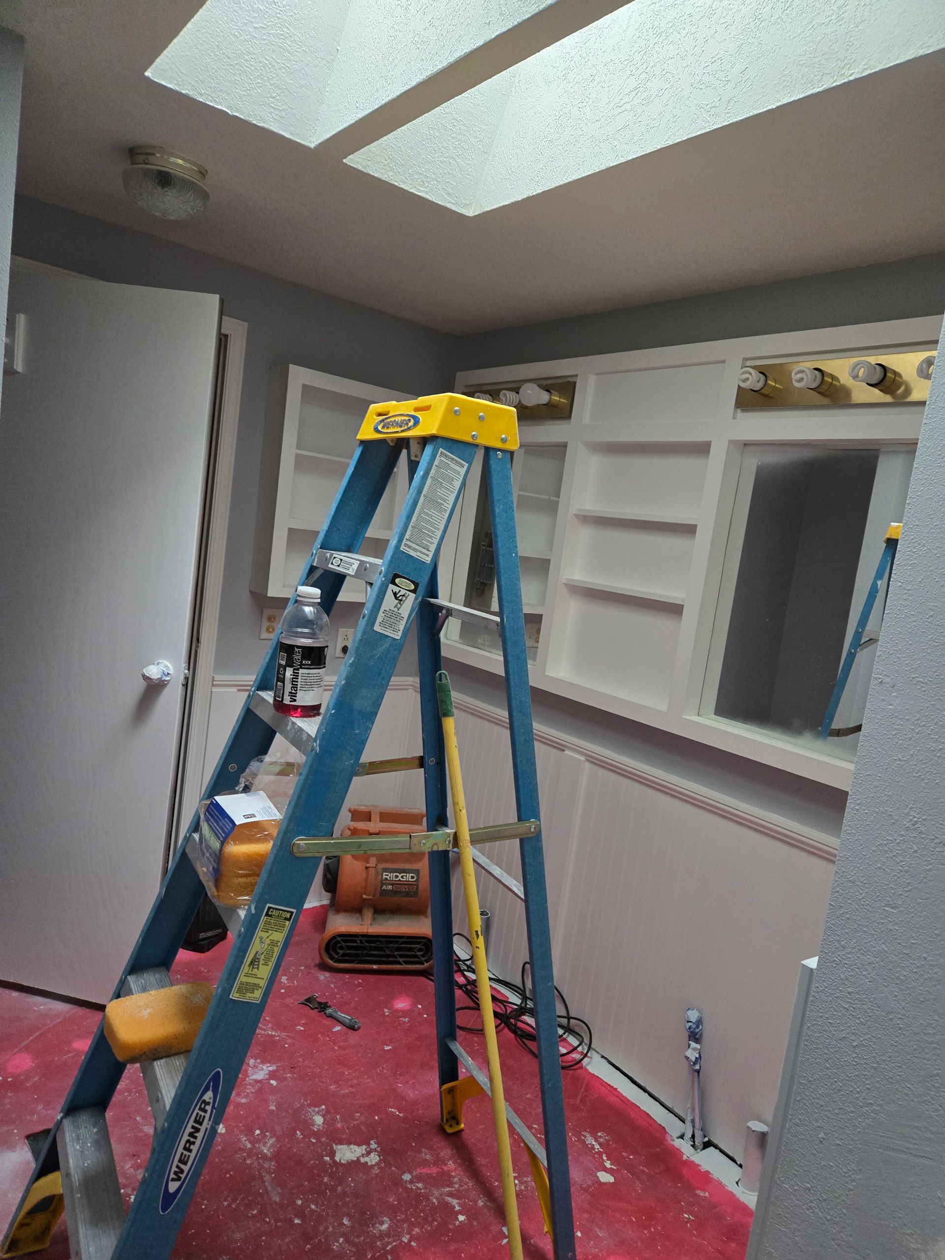Blue ladder in a room under renovation with a skylight, white shelves, and pink protective floor covering