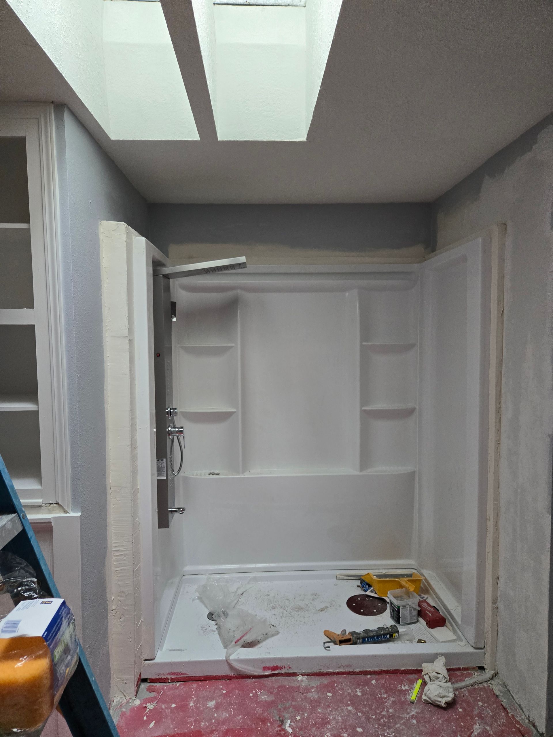 Damaged bathroom with broken sink cabinet, debris on floor, and exposed shelves under bright ceiling lights