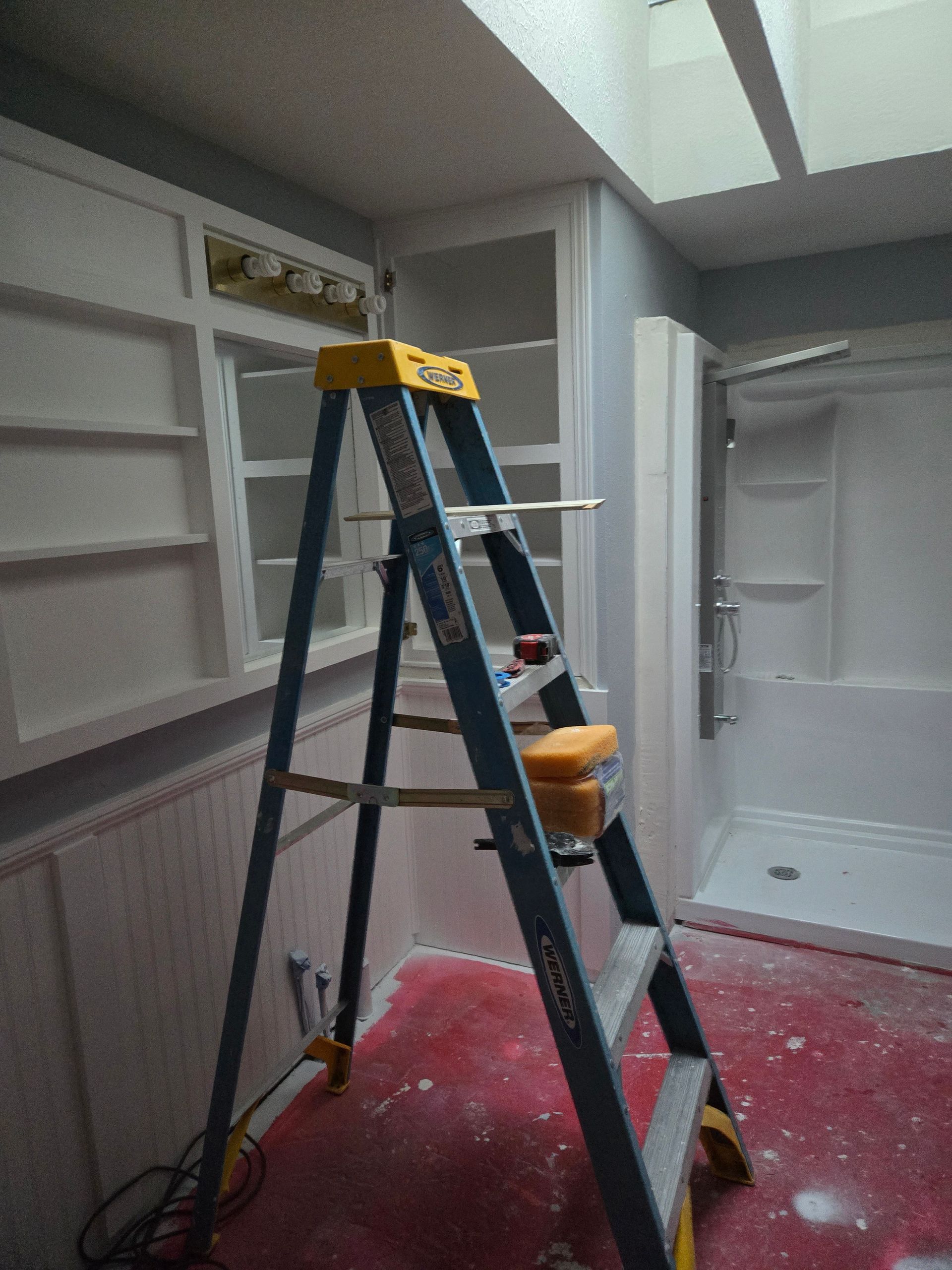 Step ladder on red-covered floor in a room with white walls and built-in shelving.