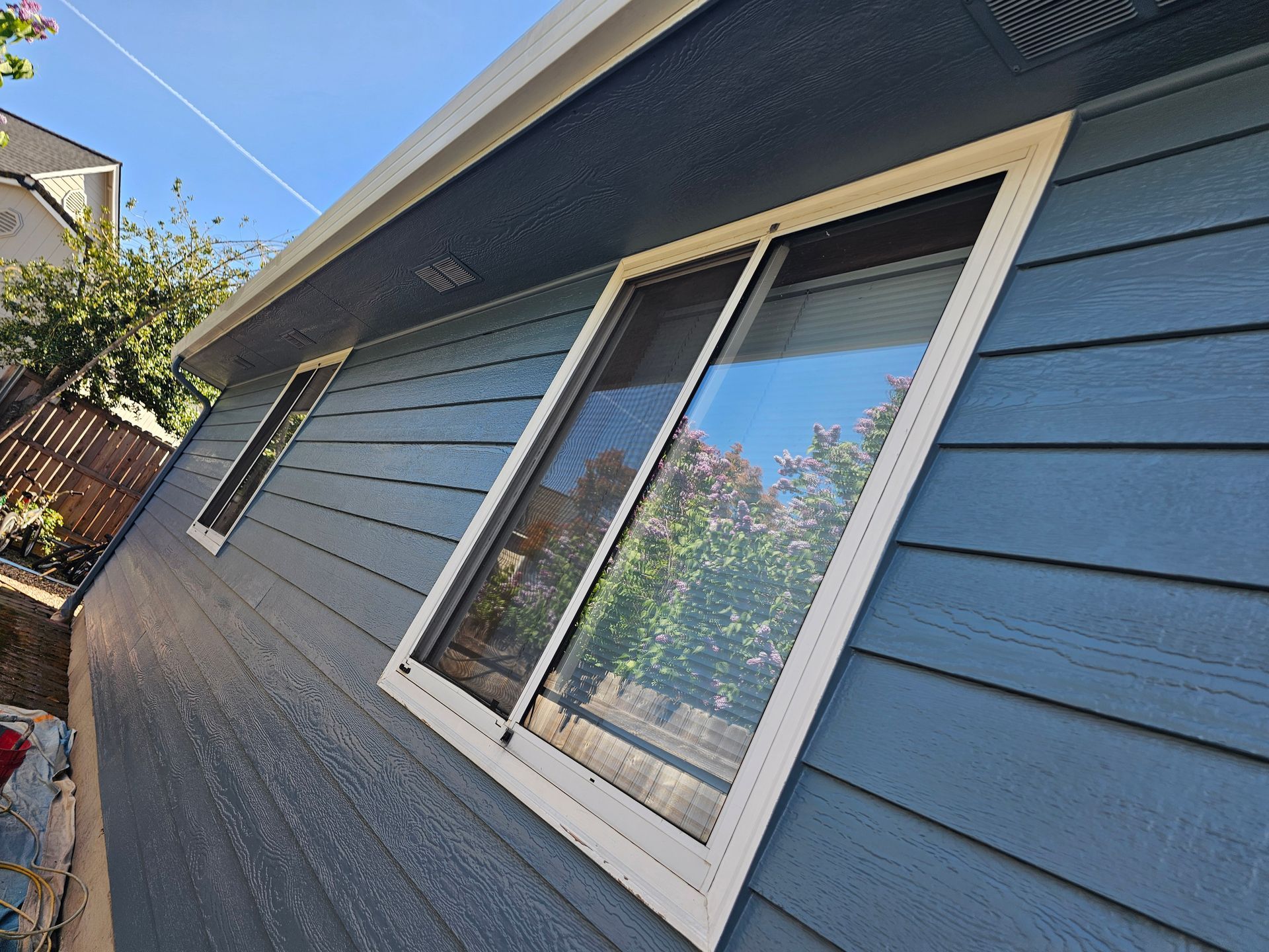 Blue house exterior with white-trimmed windows and slanted siding in bright sunlight