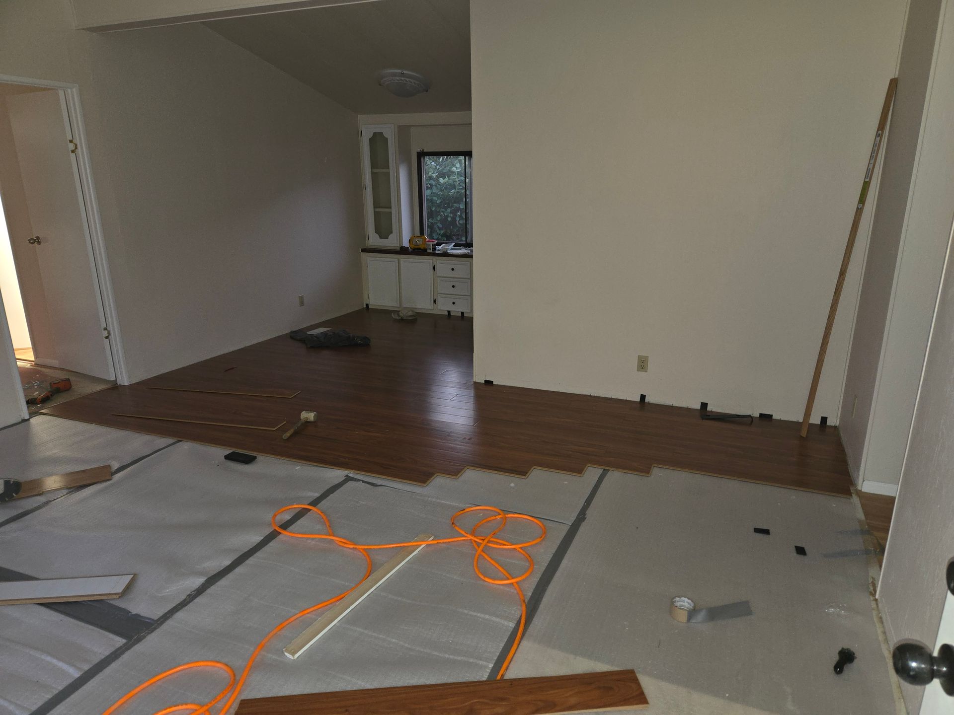 Partially renovated empty room with exposed flooring, white walls, and orange extension cords across the floor
