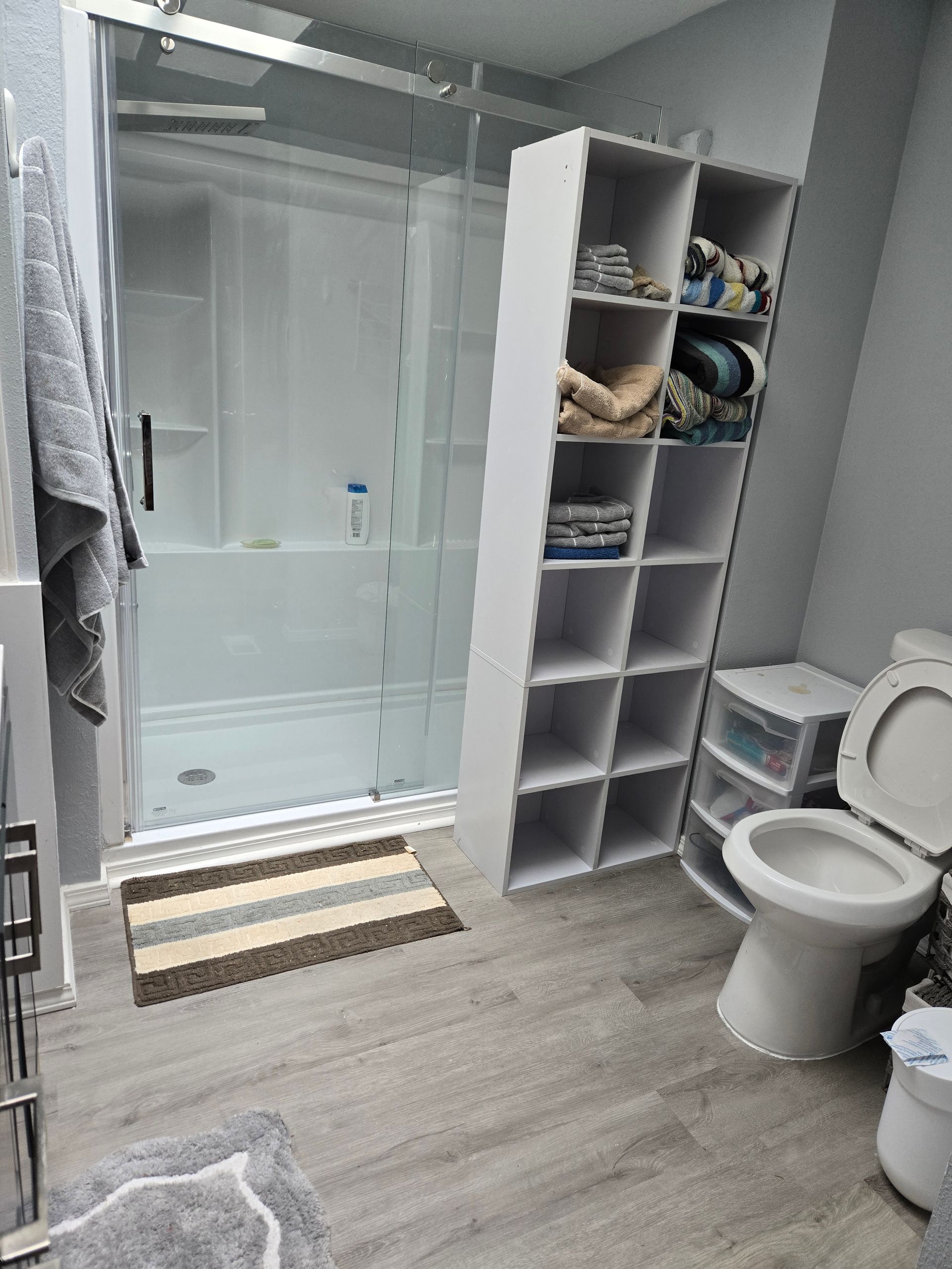 Bathroom with glass shower, open shelving, toilet, and gray wood-look floor