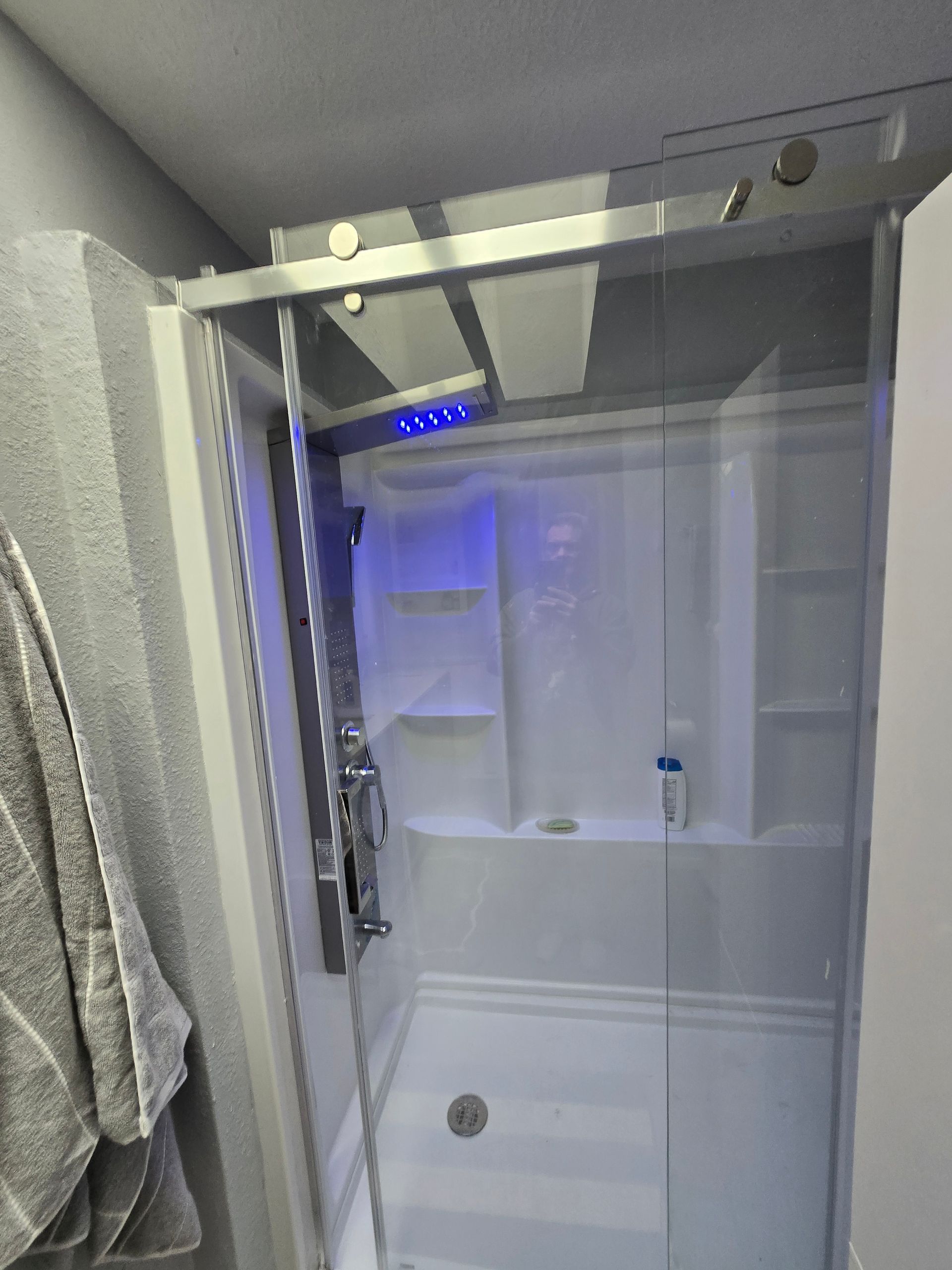 Small bathroom with a glass shower stall, chrome fixtures, white tile, and a towel hanging on the left wall.