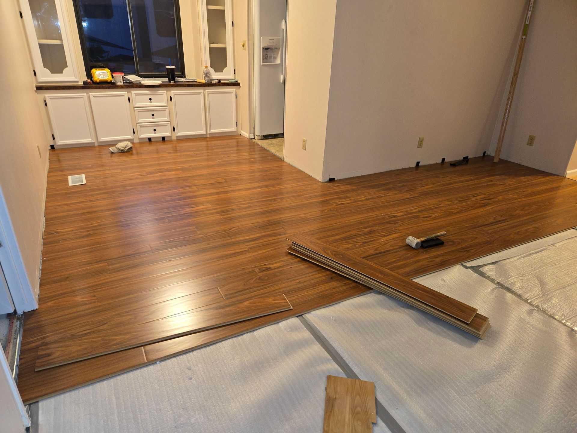 Partially renovated room with wood floor, white cabinets, and tools on a protective floor covering