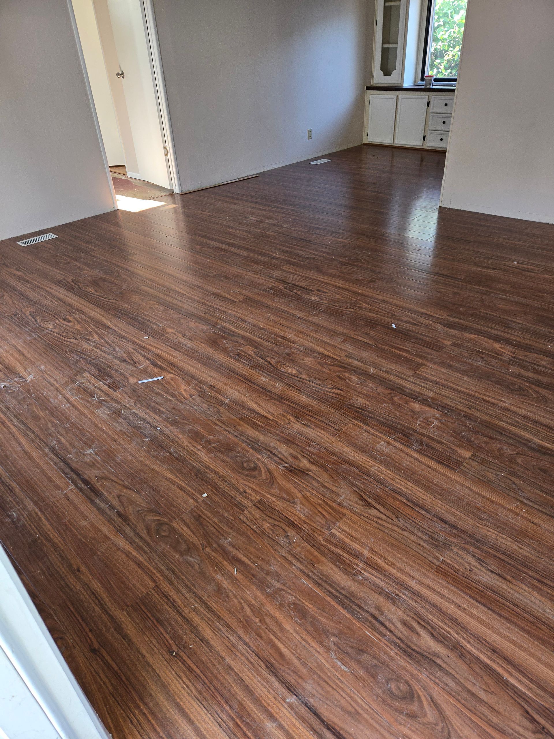 Empty room with dark wood floors and light walls, lit by daylight from a window.
