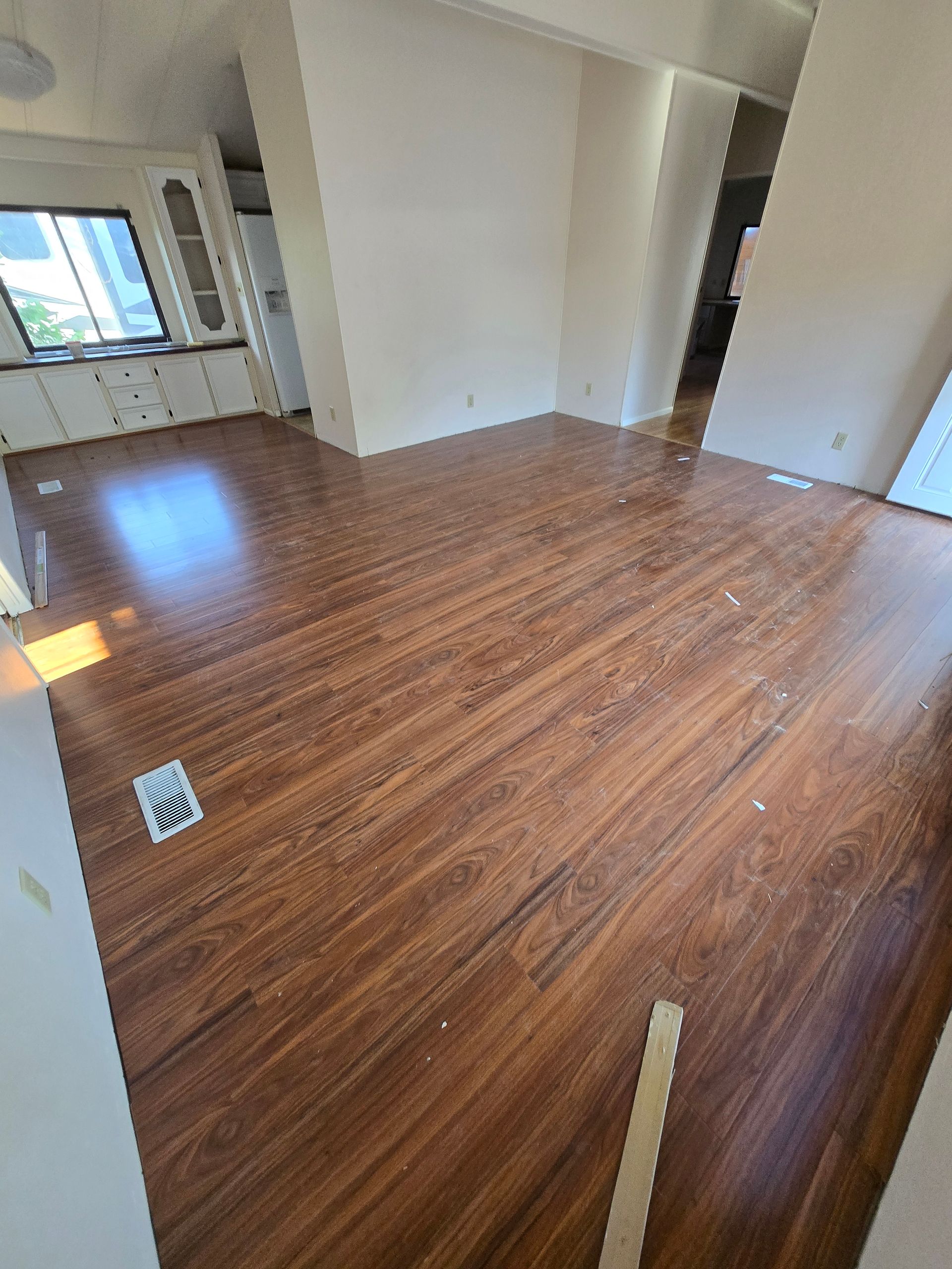 Empty room with wood-look flooring, white walls, and bright windows.