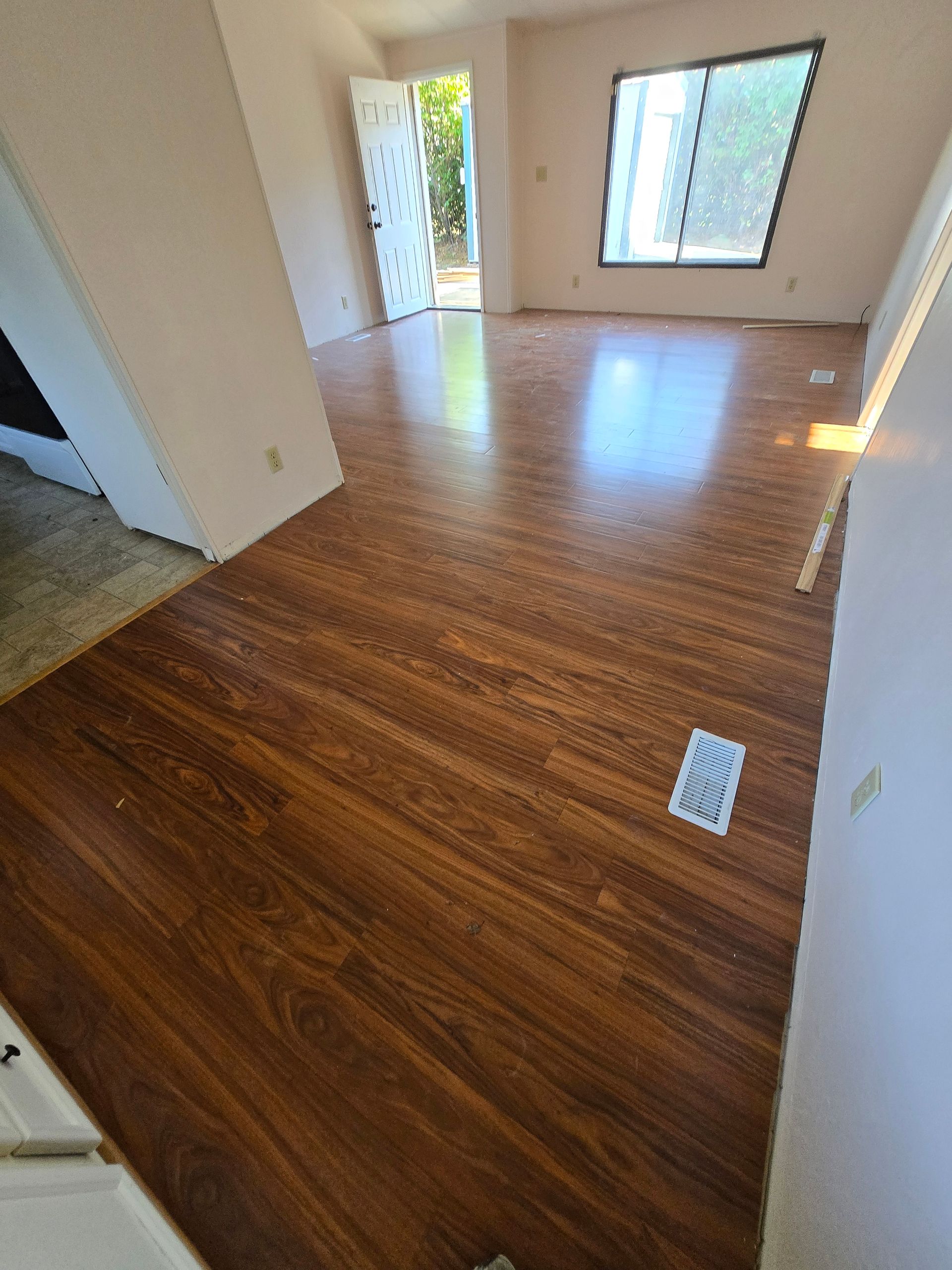 Empty room with wood-look flooring, white walls, and sunlight from a large window.