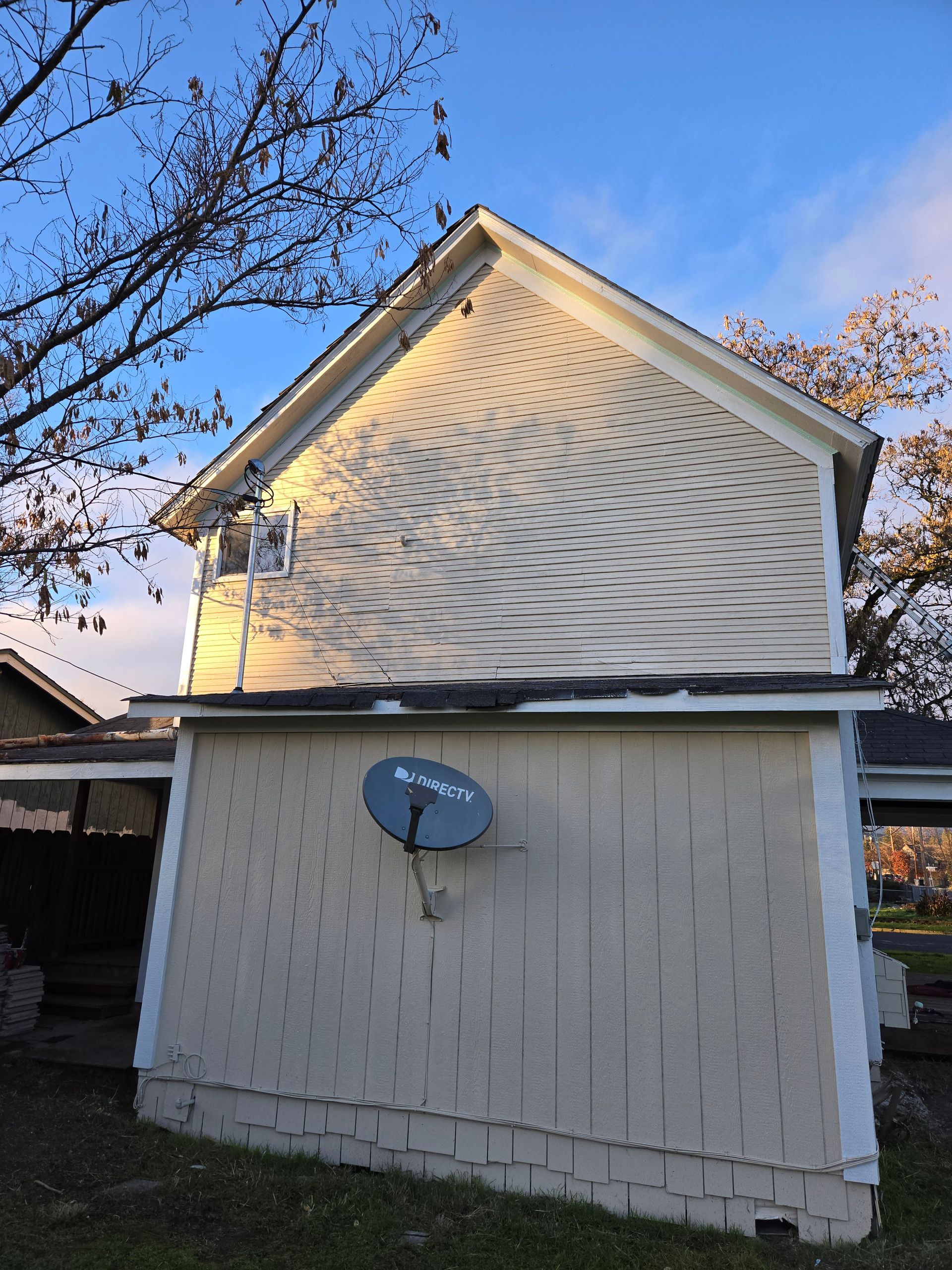 Tan-sided house with a blue satellite dish on the exterior, viewed from the side under a blue sky