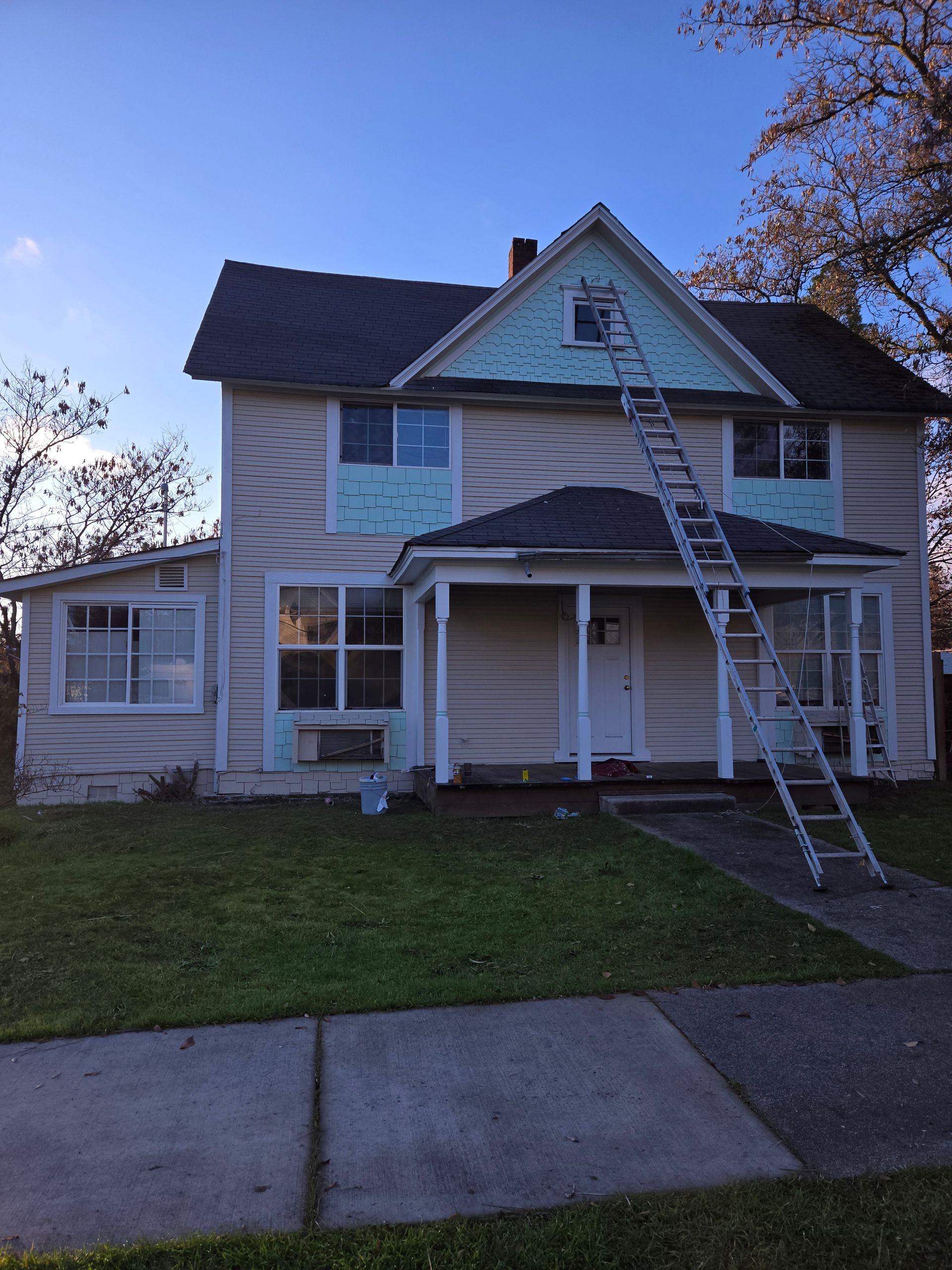 Old two-story house with peeling paint and a ladder leaning against the front porch at dusk