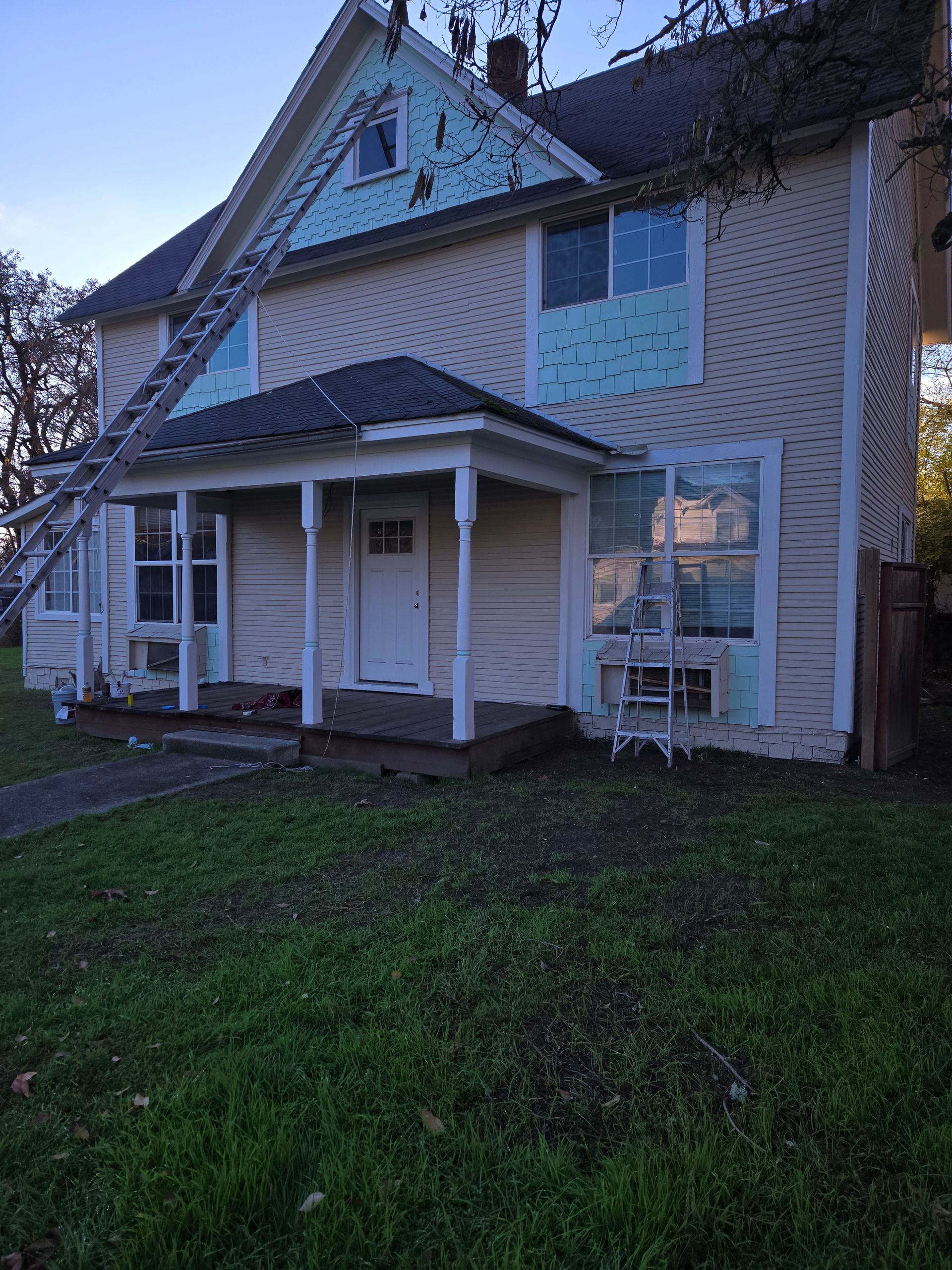 Two-story beige house with a small front porch and green lawn at dusk