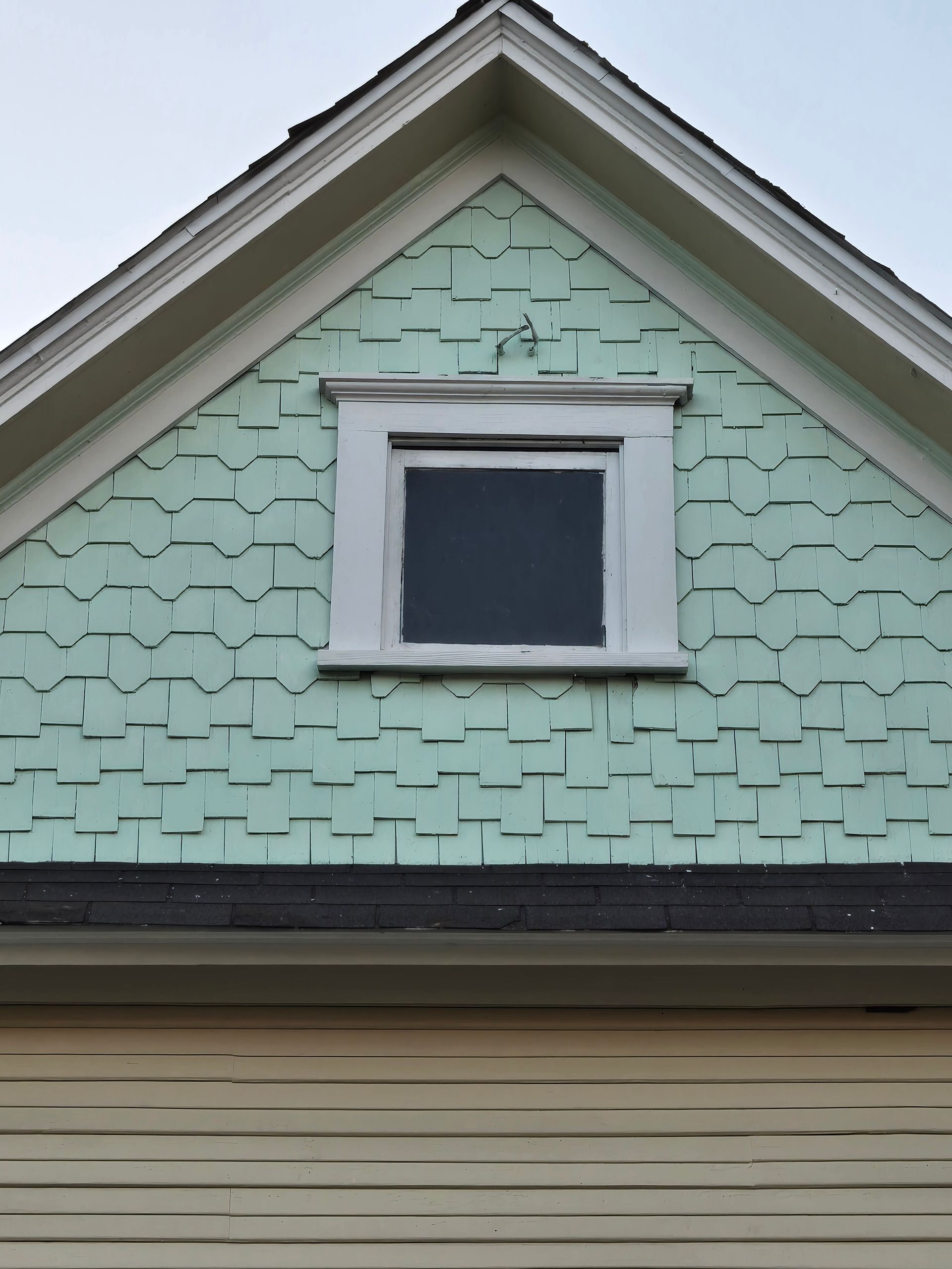 Mint-green house gable with white trim and a small central window above beige siding