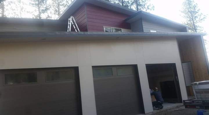 Front of a beige house with a dark garage door and a person standing near the doorway