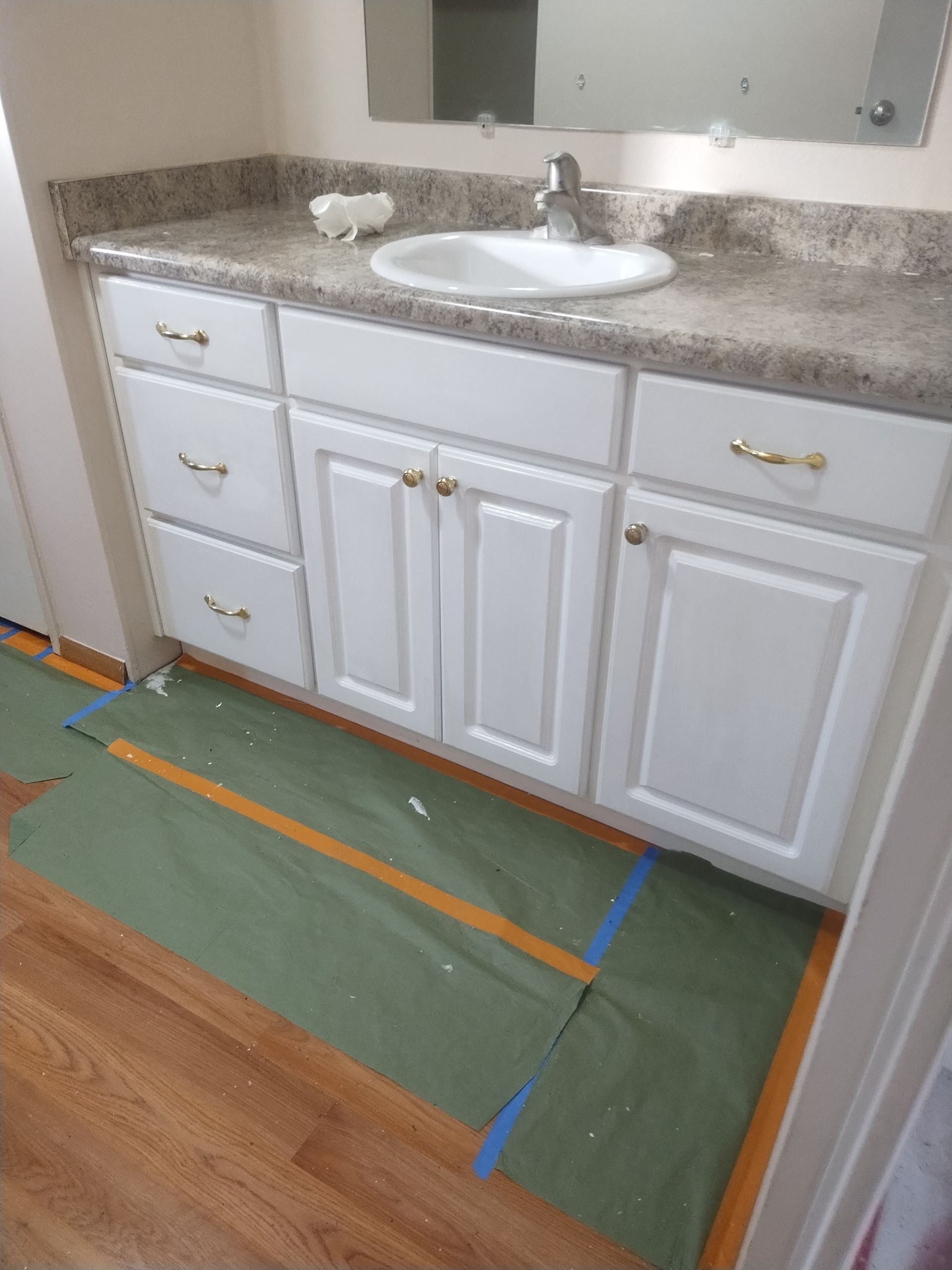 Bathroom vanity with white cabinets, beige countertop, and green floor covering taped down for work.