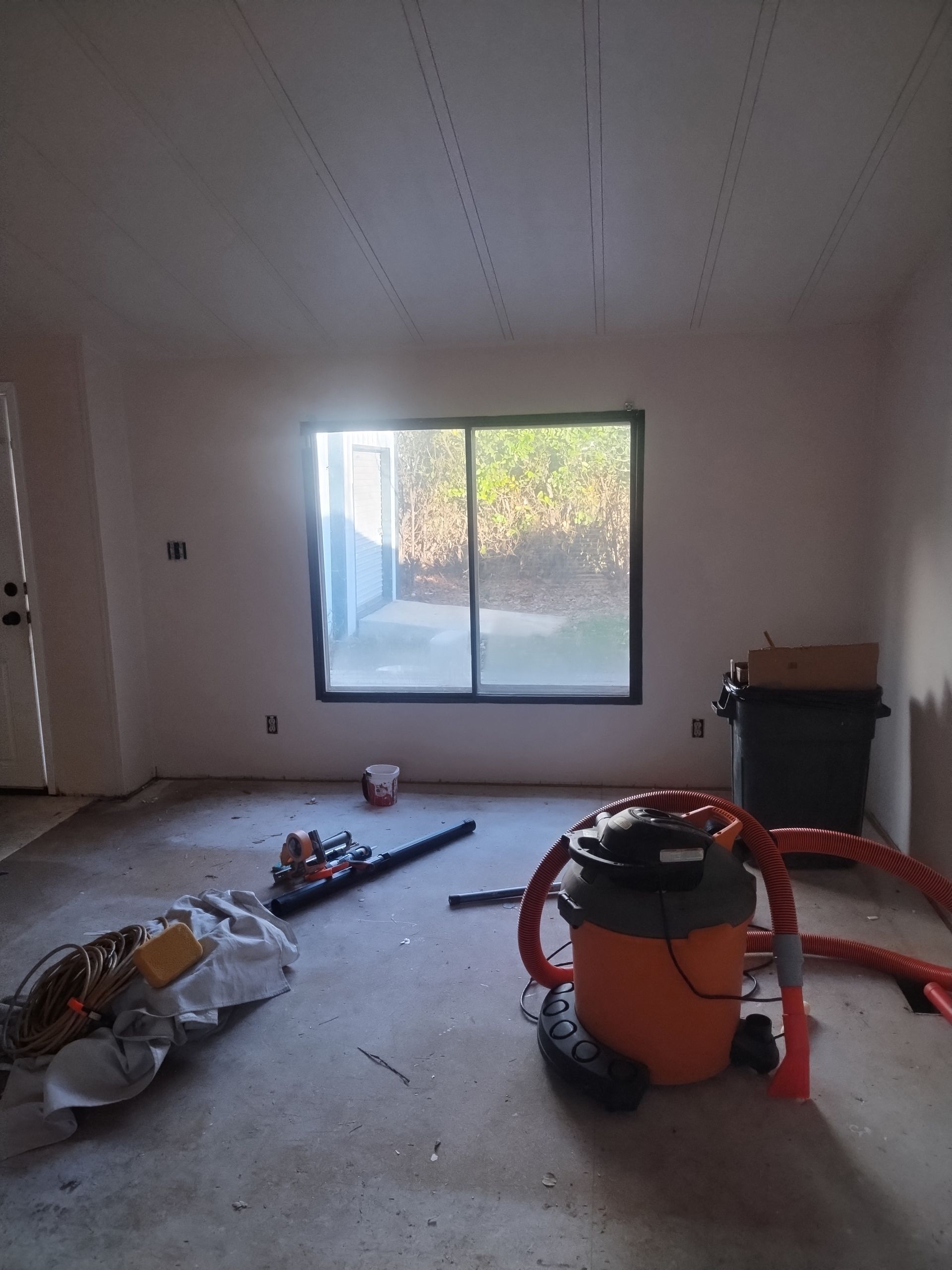 Messy room under renovation with tools, debris, and a large window letting in daylight.