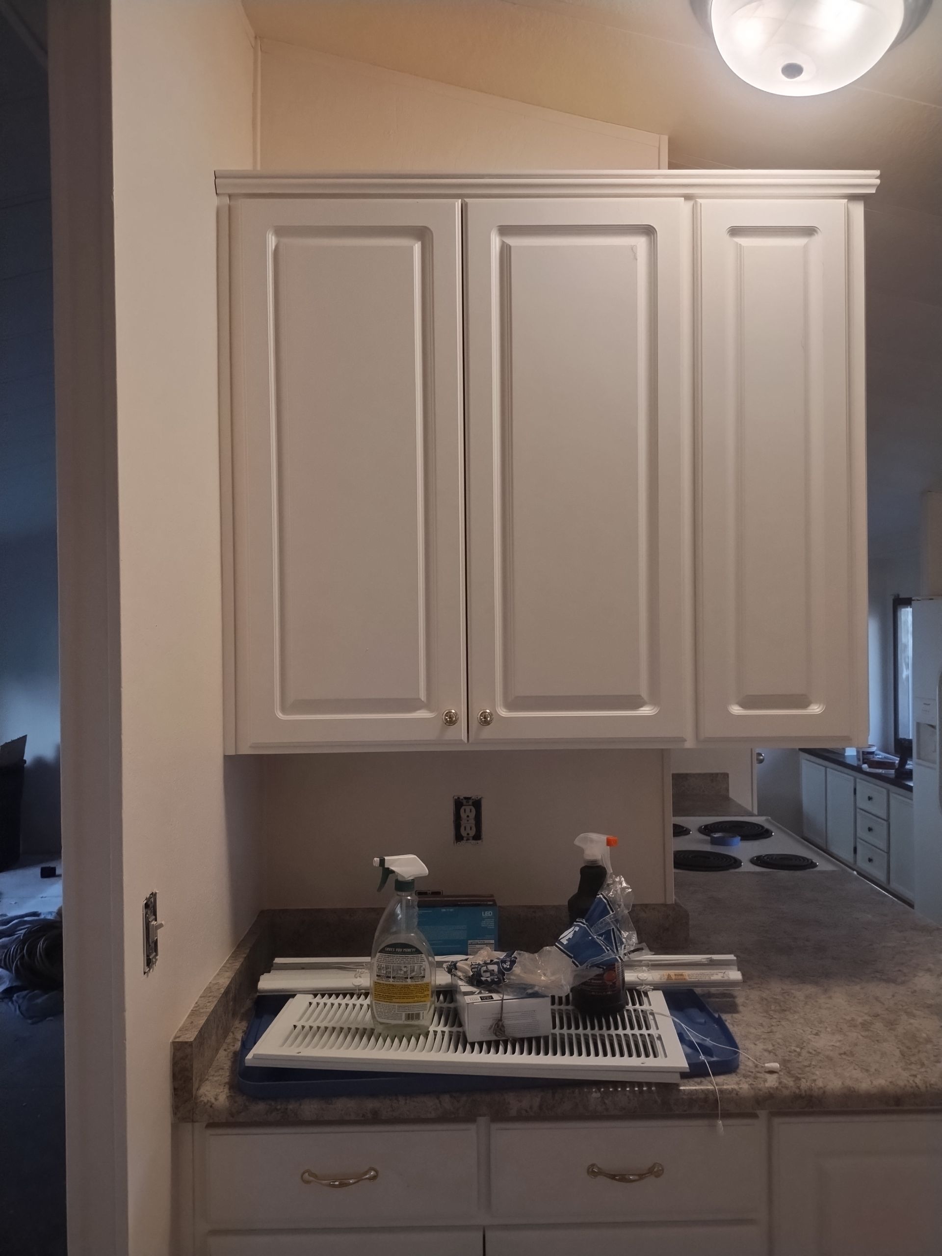 Kitchen with white cabinets and a countertop covered in cleaning supplies and tools