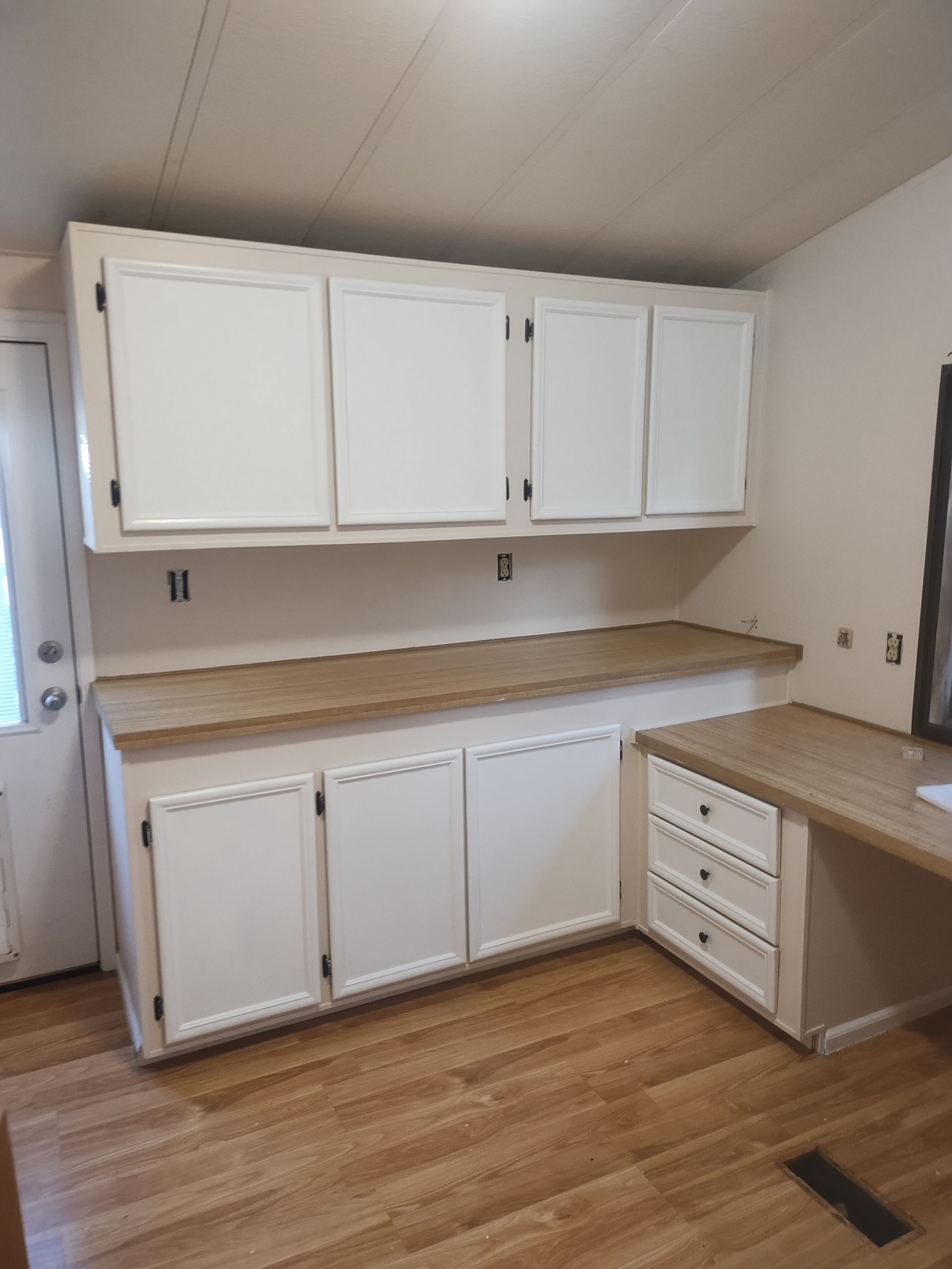 Empty white kitchen with upper and lower cabinets, wood countertops, and hardwood floors