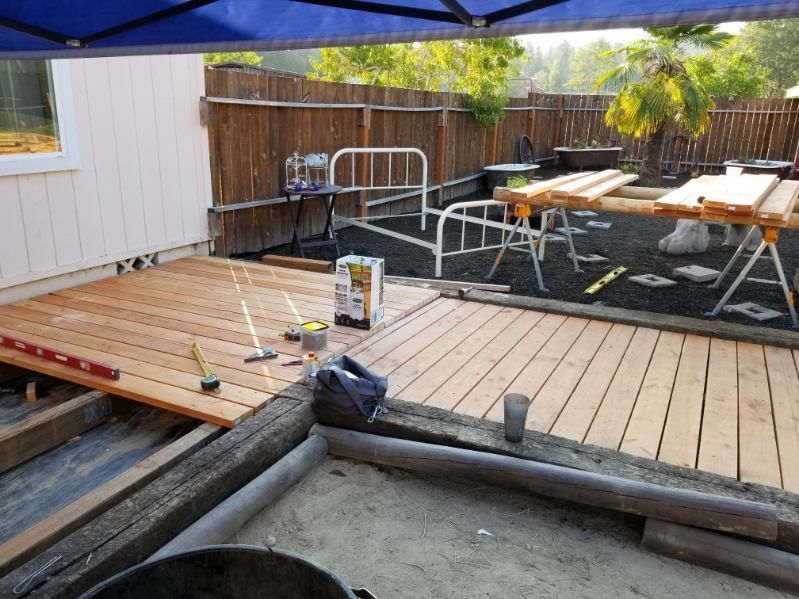 Backyard deck under blue canopy, with patio furniture and a few tools on wooden planks.